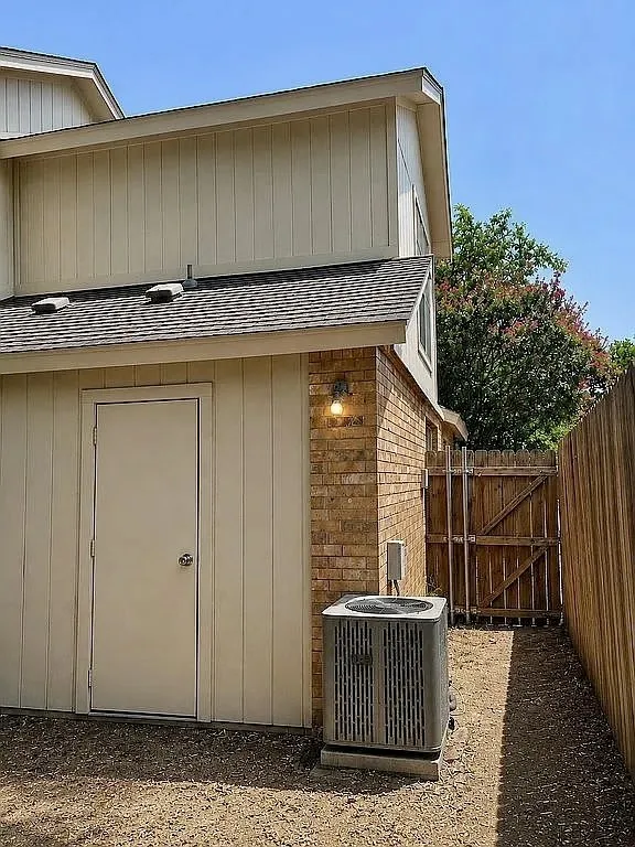 Exterior featuring brick accents, vertical siding, a composition shingle roof, and a wood fence
