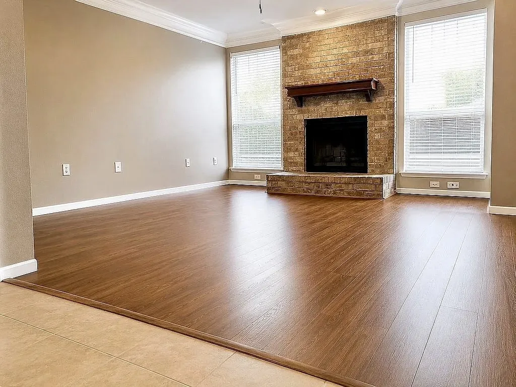 Brick-surround fireplace with a wood mantle, wood-finish flooring, crown molding, and multiple windows with blinds