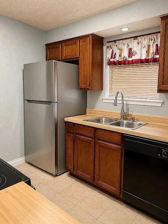 Kitchen featuring rich wood-finish cabinetry, a dual-basin stainless steel sink with a gooseneck faucet, light-toned countertops, and tiled flooring