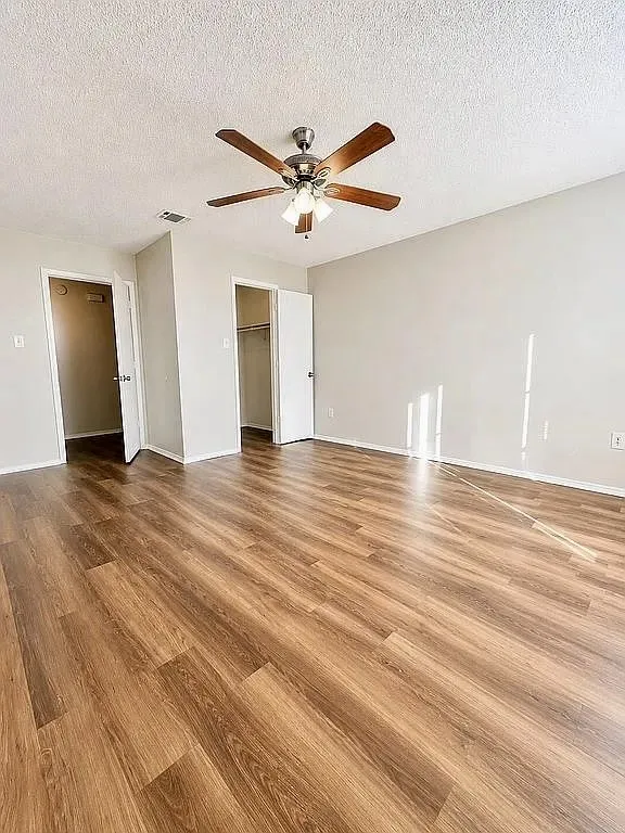 Spacious room featuring wood-finish flooring, a ceiling fan with integrated lighting, and neutral wall paint