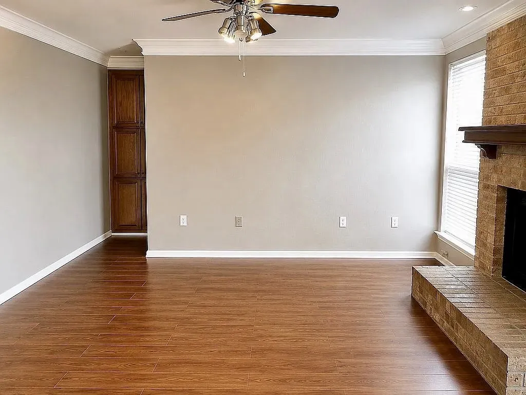 Wood-finish flooring, built-in cabinetry, brick fireplace with wood mantel, crown molding, and a ceiling fan