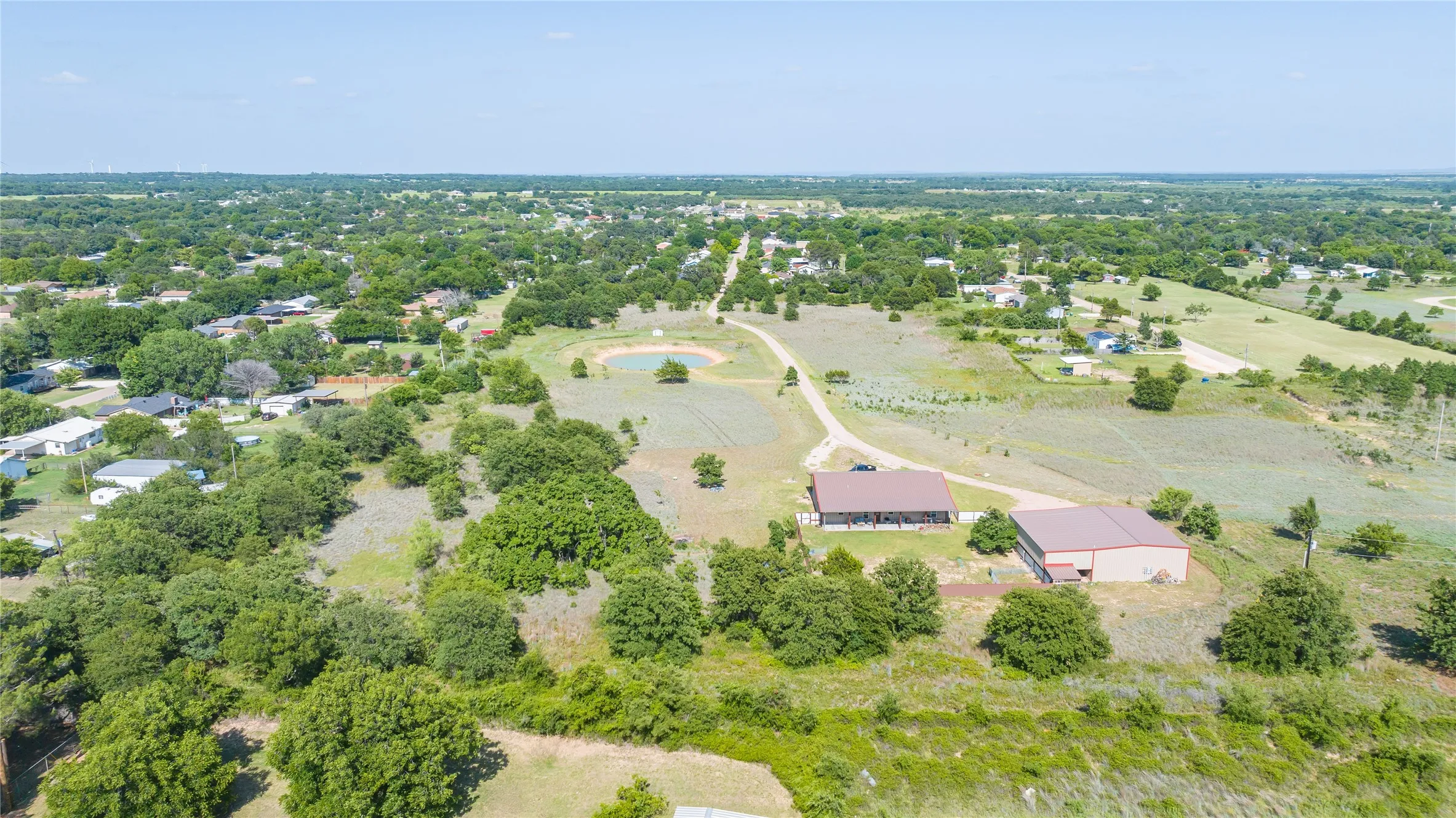 Expansive property featuring mature trees, open land, a visible pond, and two utility buildings