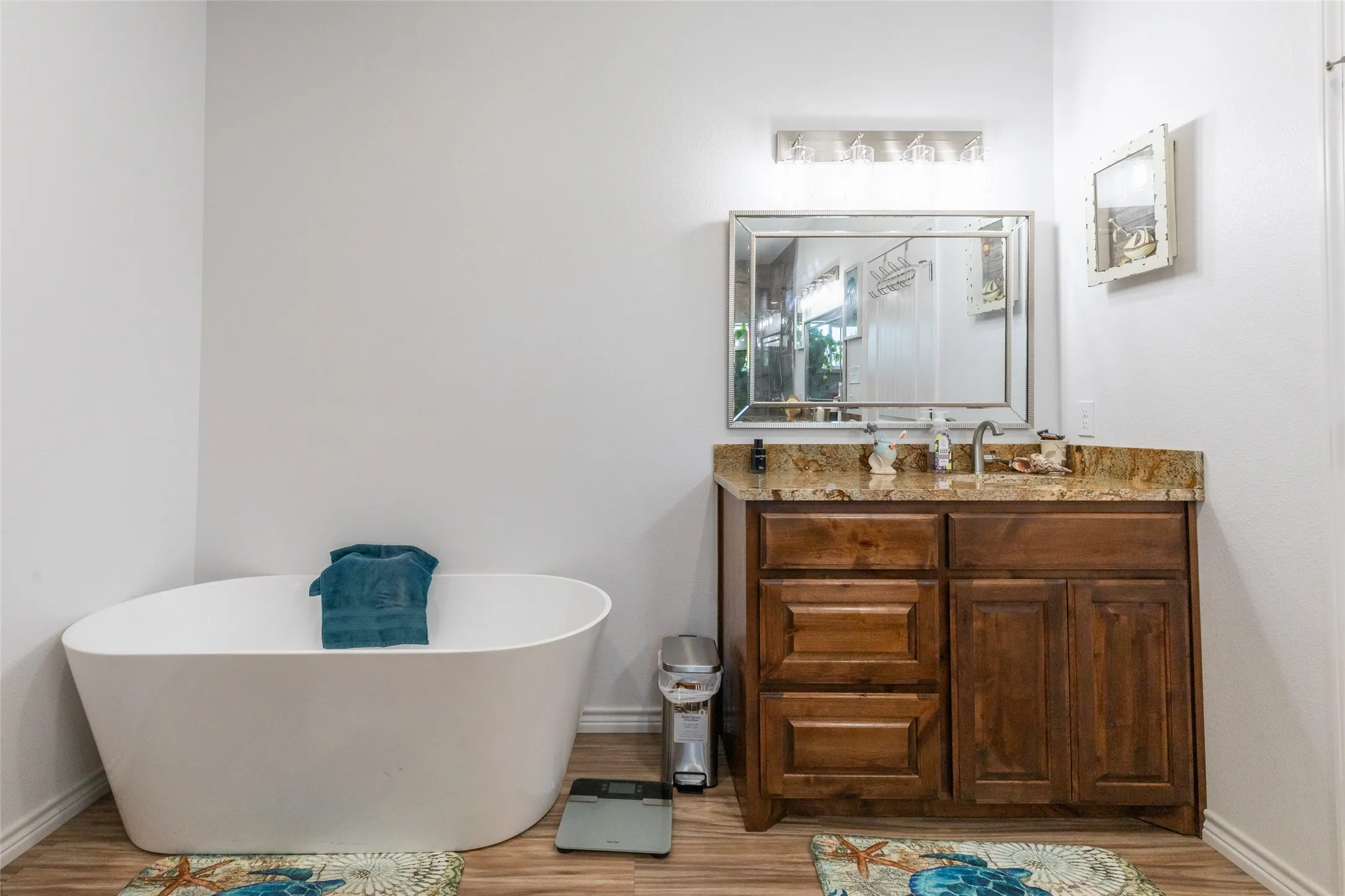 Spa-inspired primary bathroom featuring a freestanding soaking tub with clean-lined silhouette, wood-finish cabinetry with multiple storage drawers, and a warm-toned stone countertop