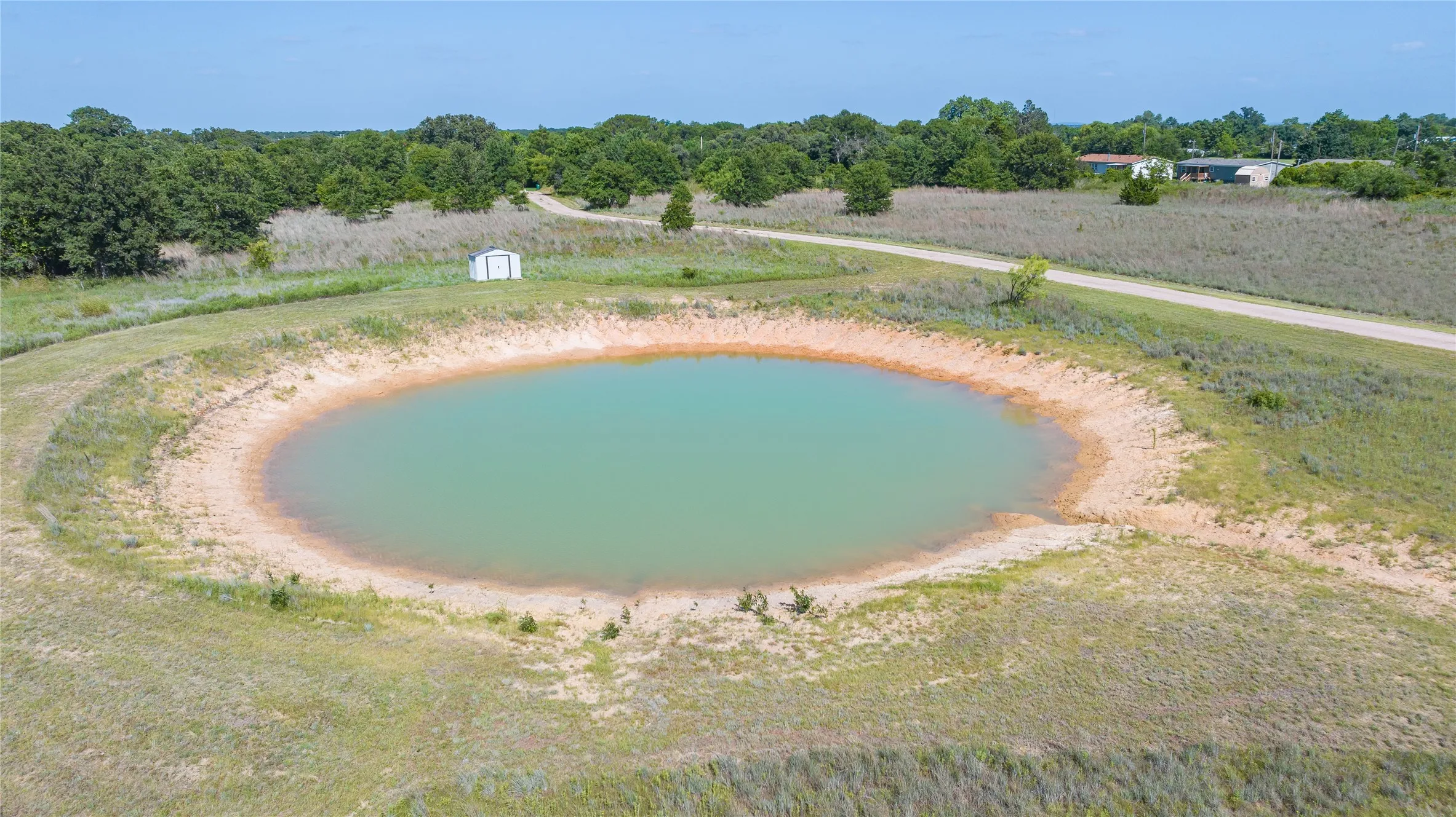 Expansive property featuring a tranquil pond, surrounding natural landscape, and a gravel road