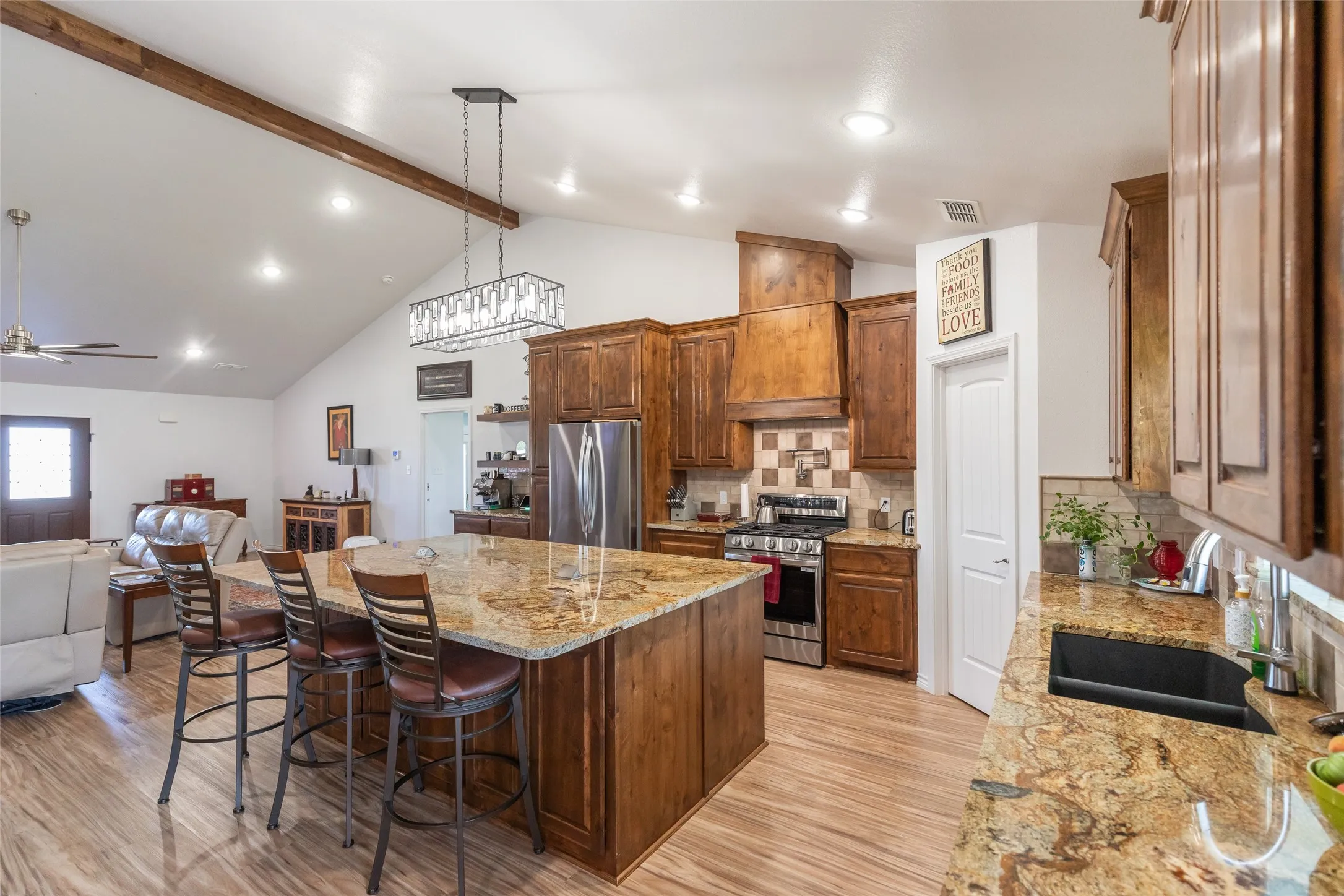Kitchen featuring an island with stone countertop, wood-finish cabinetry, stainless steel appliances, and a tiled backsplash