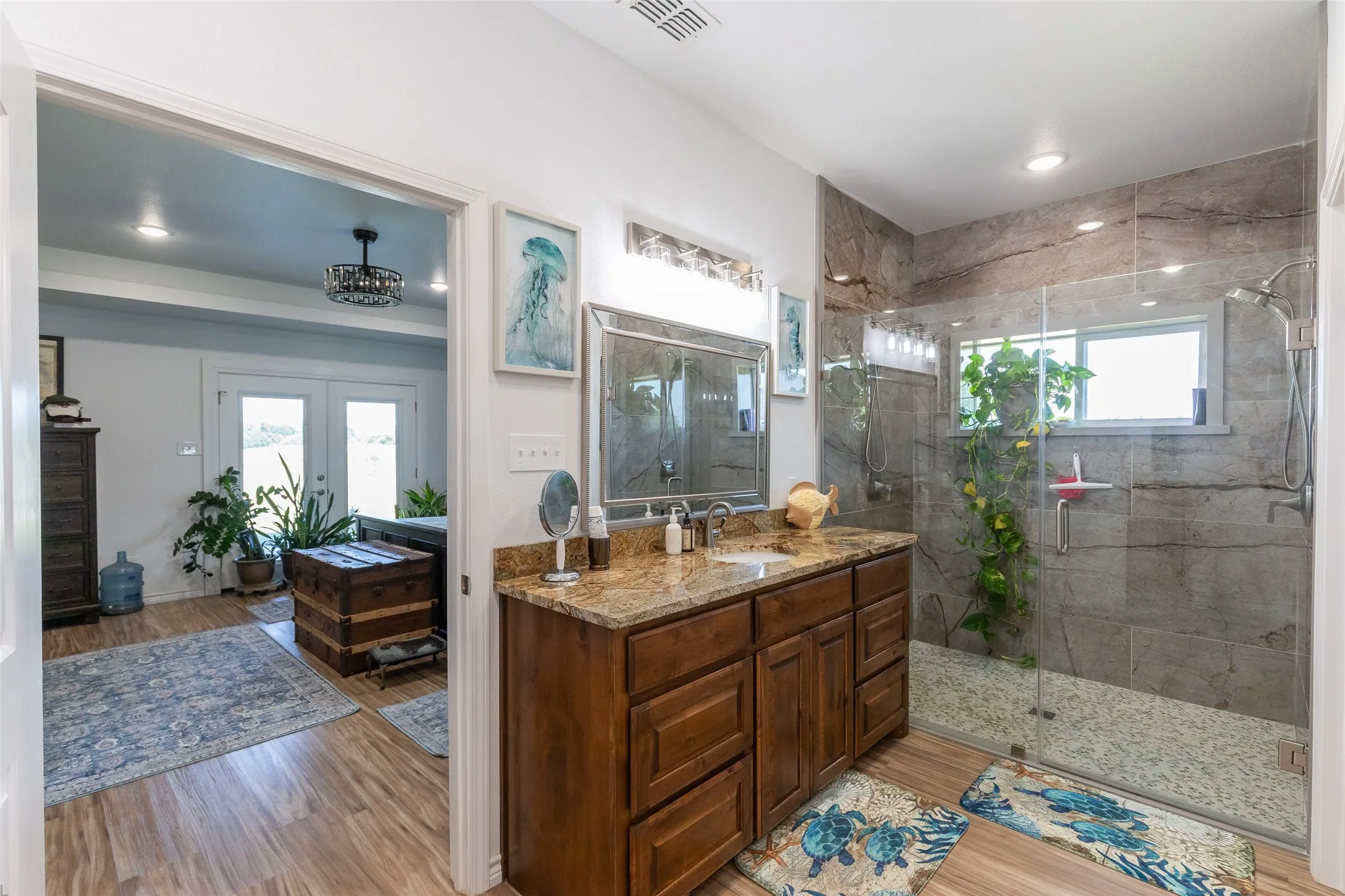 Wood-finish flooring, single vanity with a stone countertop, glass-enclosed shower with tile walls, and recessed lighting