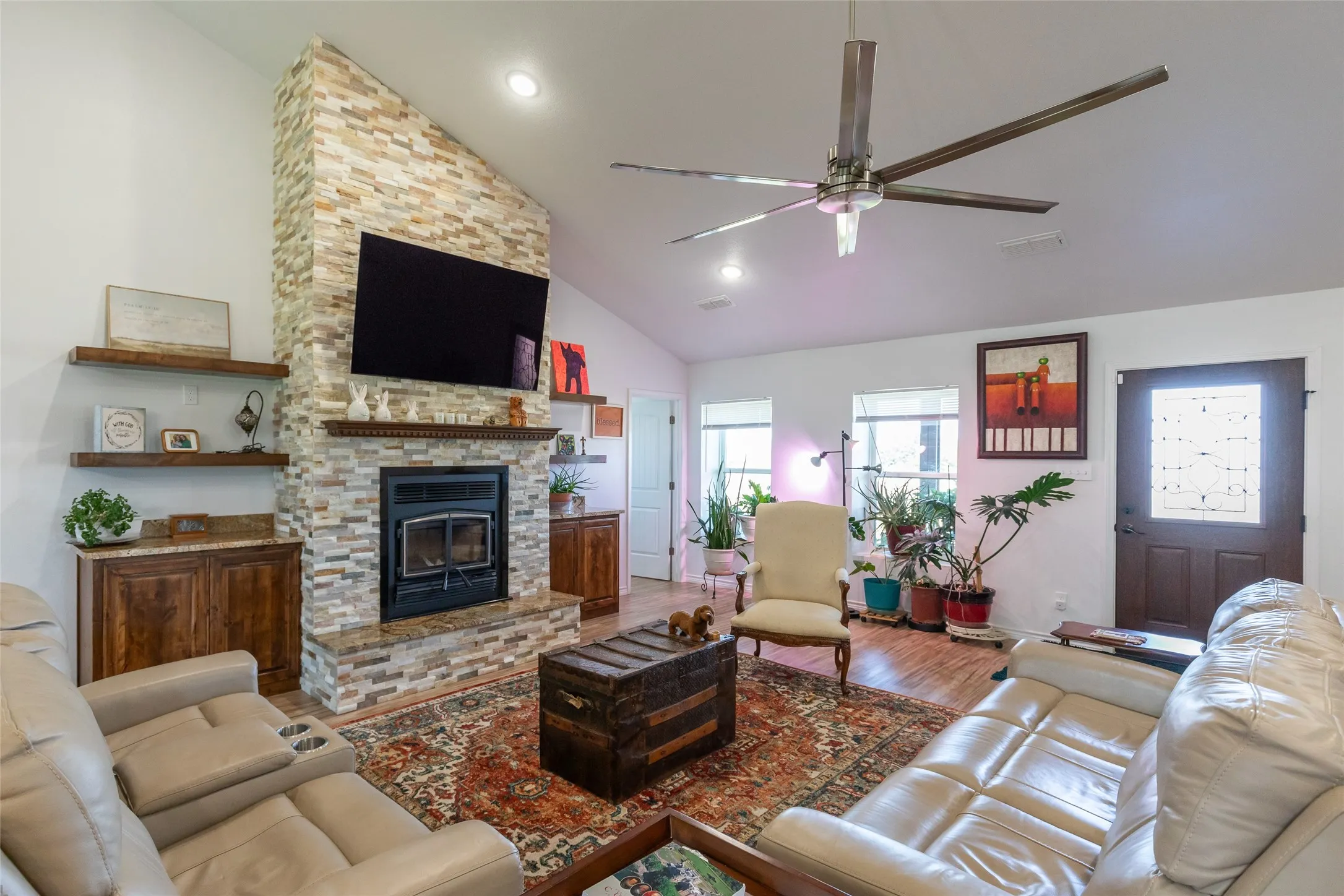 Vaulted ceiling, stone-clad fireplace, wood-finish flooring, built-in cabinetry, and ceiling fan