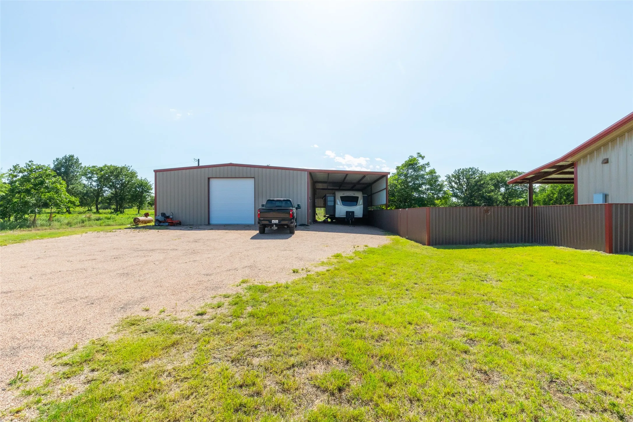 Metal building featuring a large roll-up door, an attached covered carport, and a gravel drive