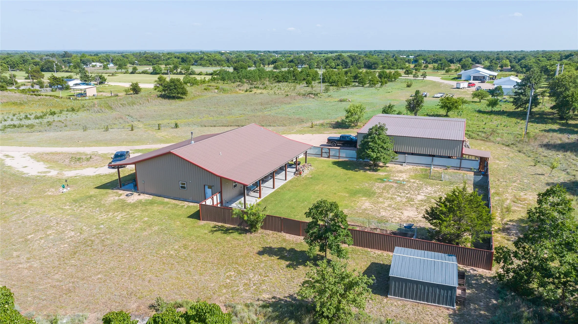 Metal-sided main residence with a covered porch, detached metal-sided outbuilding with an exterior fence, and a separate storage shed
