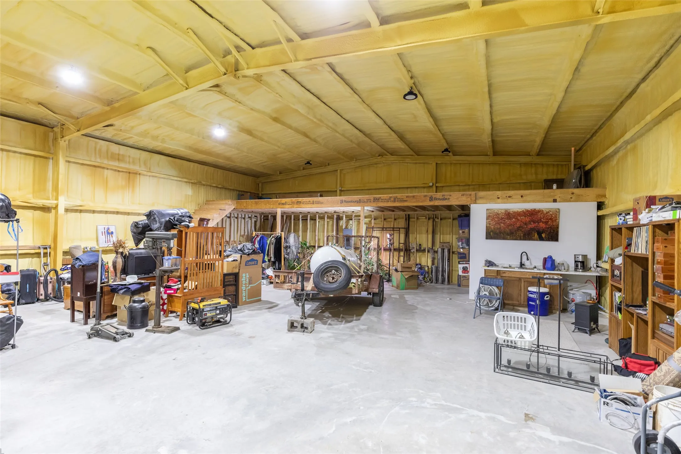 Spacious interior with high ceilings, exposed wood beams, concrete flooring, and an elevated loft area