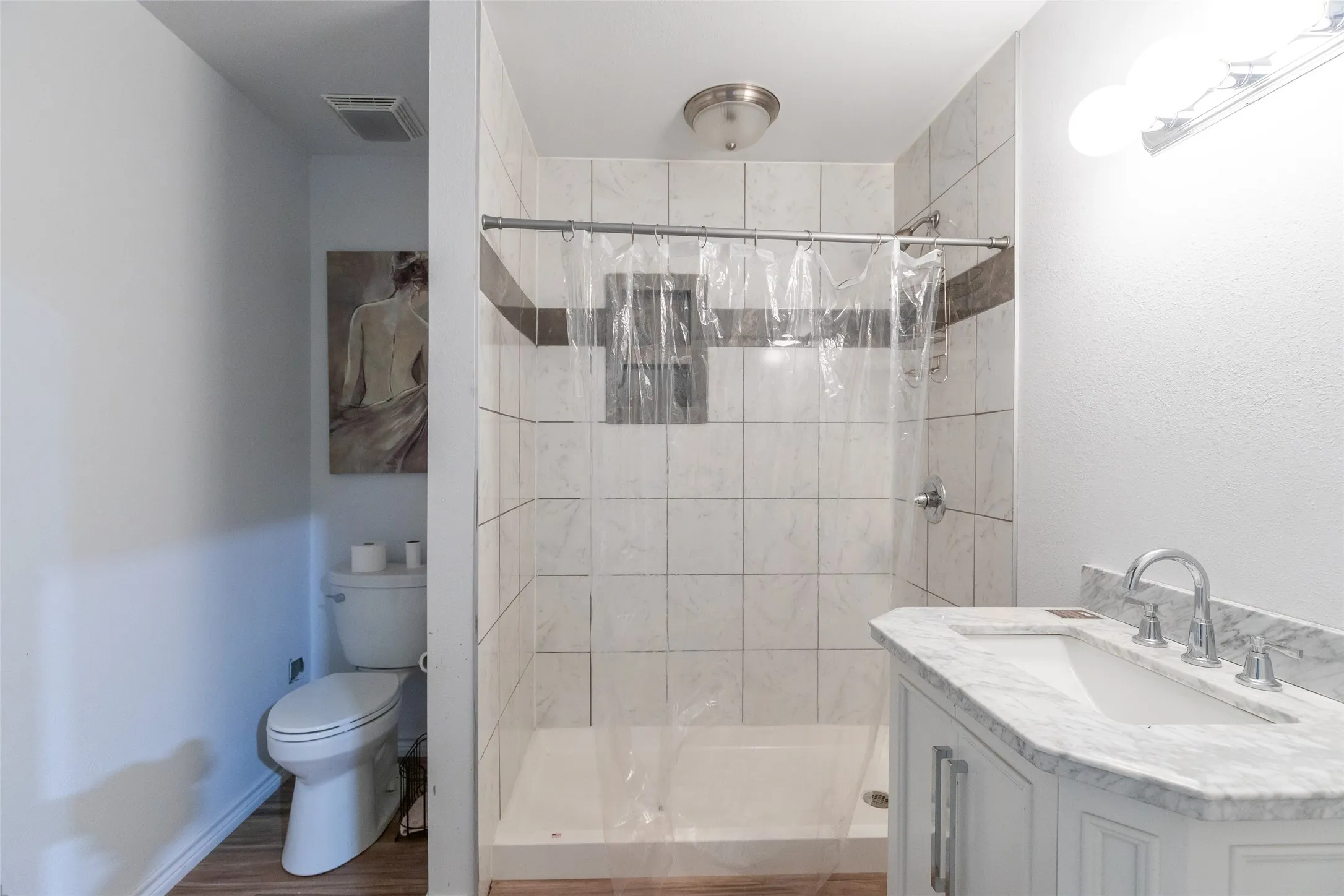 Bathroom featuring a single vanity with stone-finish countertop, ceramic tile shower surround, and wood-finish flooring