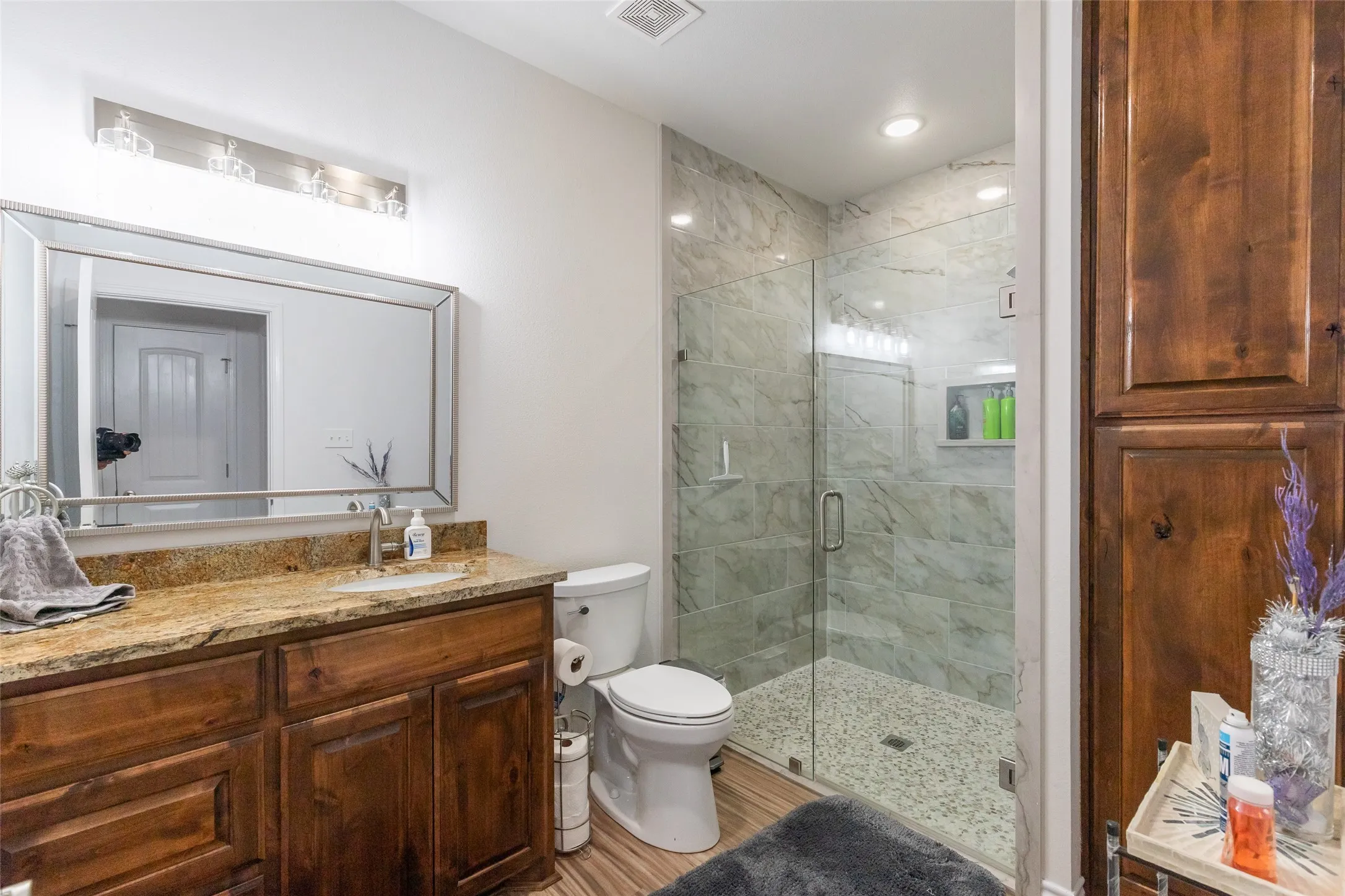 Vanity with natural stone countertop, wood-finish cabinetry, and framed mirror