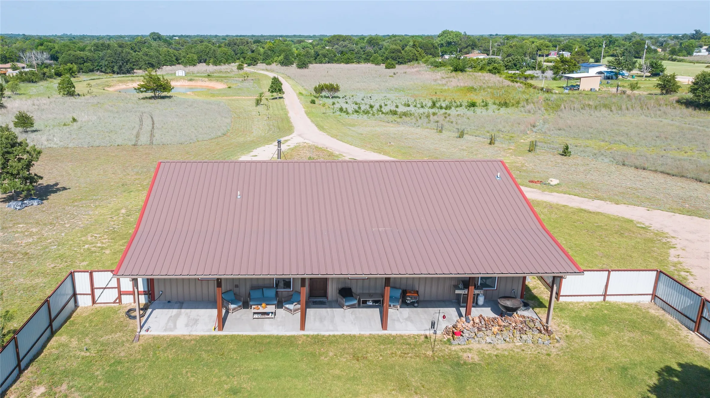 Brown metal roof with red trim, extended covered porch supported by wood columns, and a partially fenced perimeter
