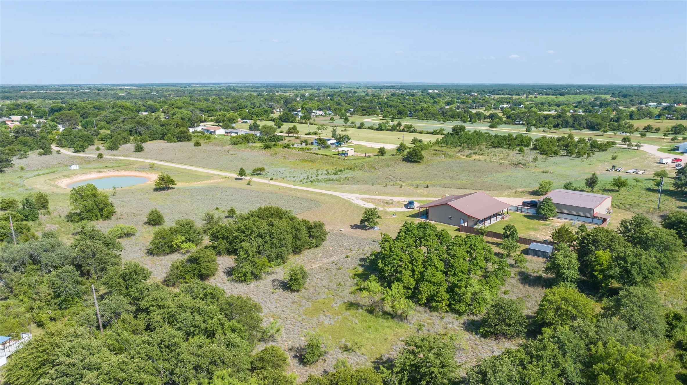 Expansive property featuring a private pond, multiple structures with metal roofs, open land, and mature trees