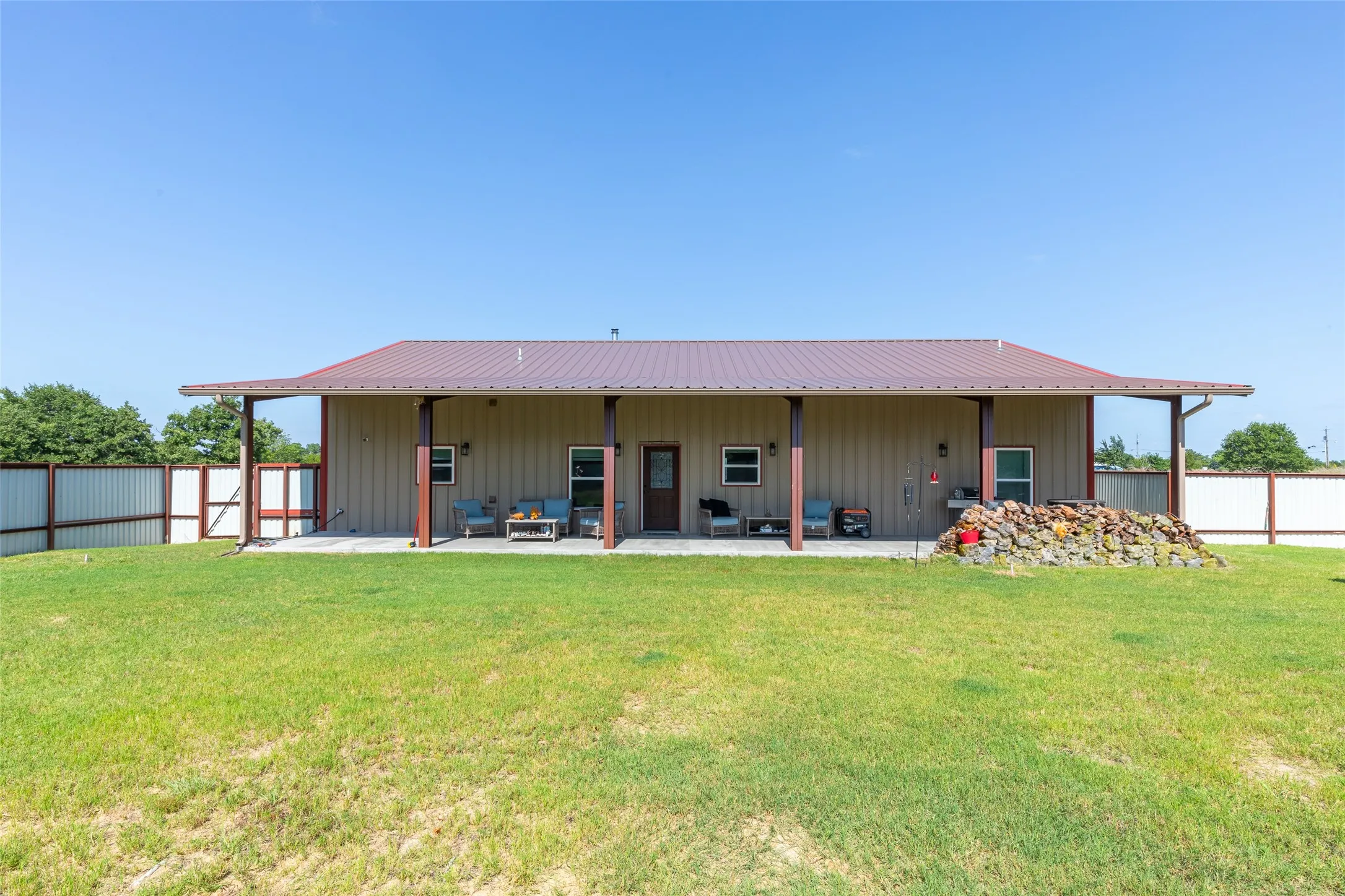 Expansive concrete patio with an extended roofline, supported by wood posts, and a full metal fence