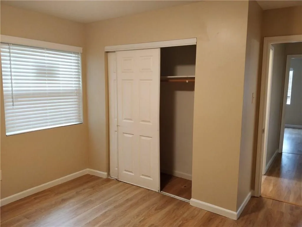 Wood-finish flooring with white baseboards, a window with blinds, and a built-in closet with sliding doors and interior shelving