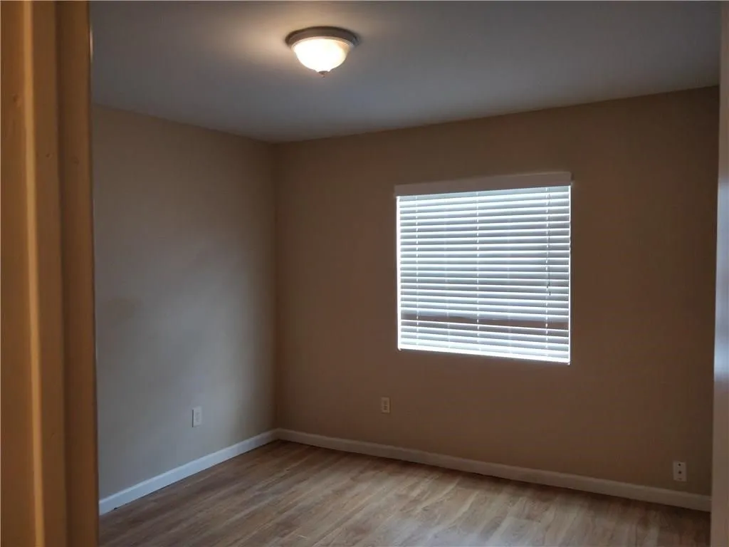 Wood-finish flooring, neutral wall tones, white trim, window with horizontal blinds, and a flush-mount ceiling light