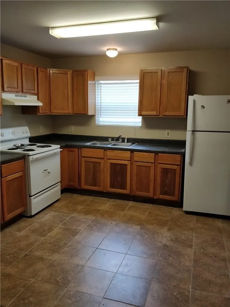 Kitchen featuring wood cabinetry, laminate countertops, a double basin sink, and tile flooring