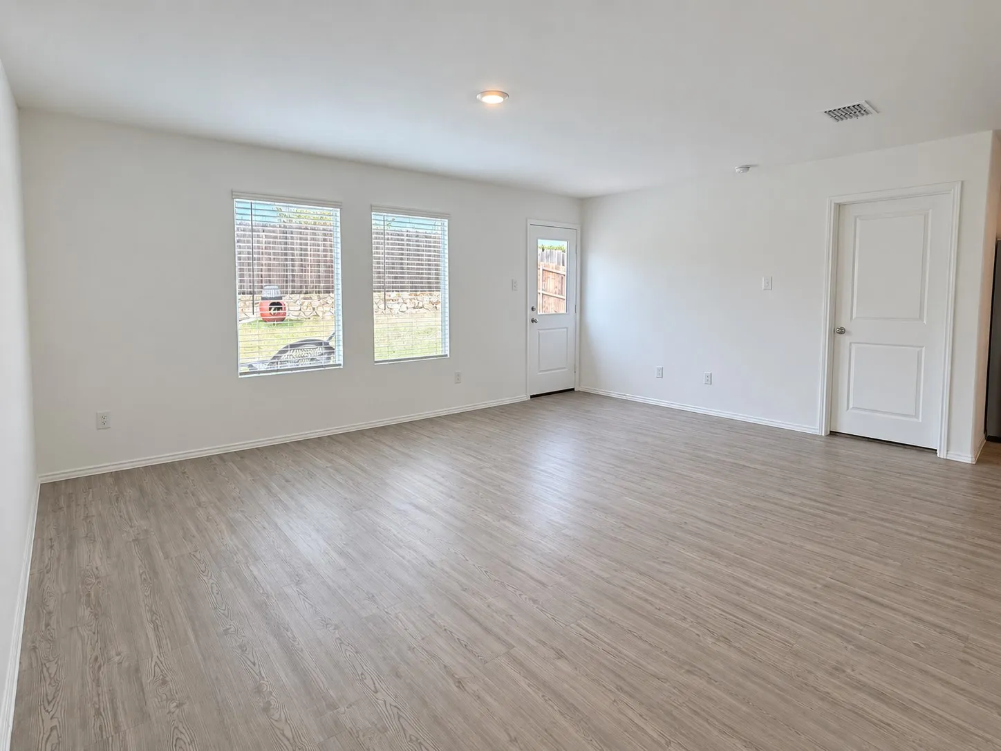 Spacious living area featuring luxury vinyl plank flooring, recessed lighting, abundant natural light, and direct access to the backyard.