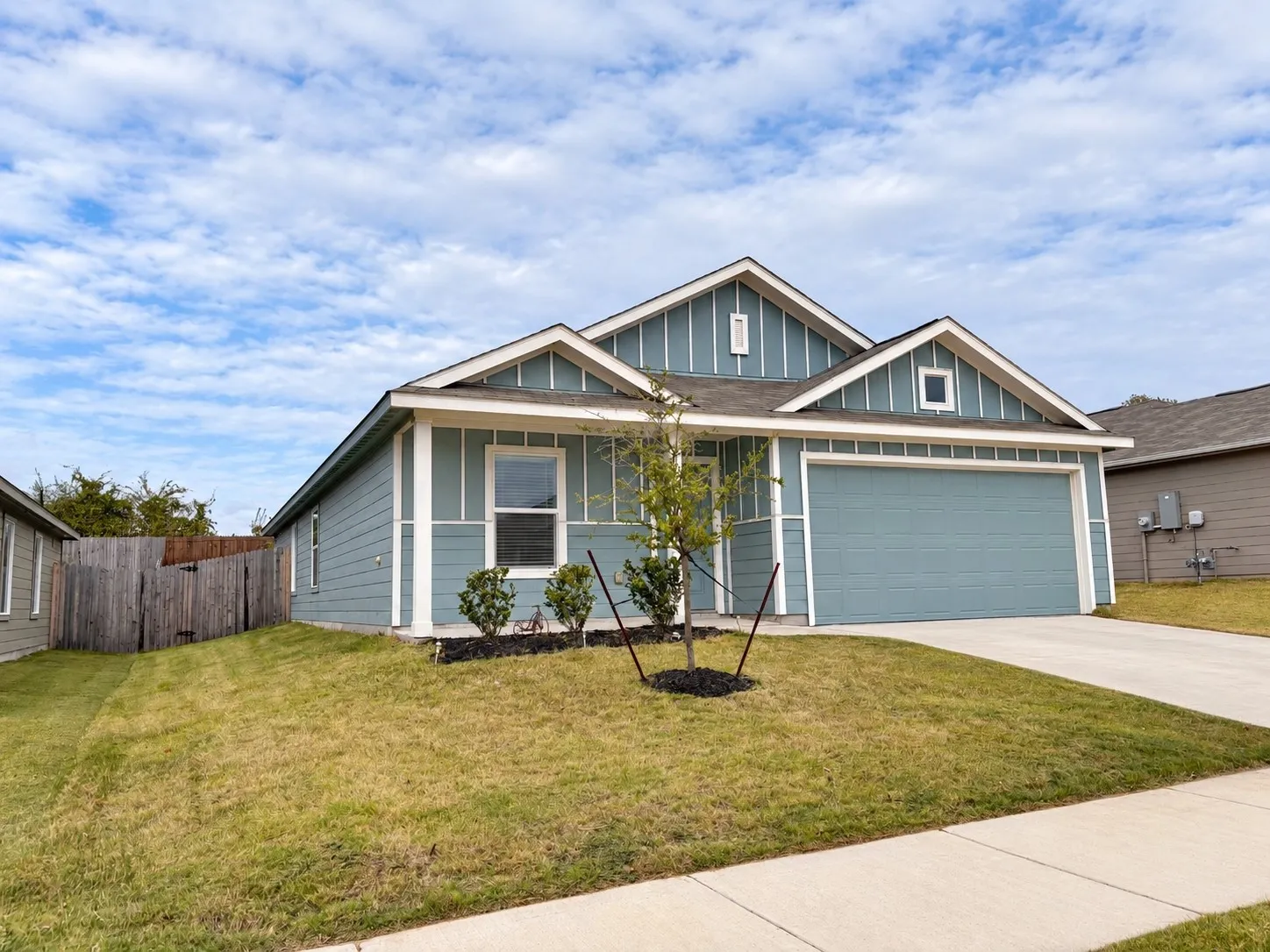 Attractive single-story home featuring blue siding with crisp white trim, an attached two-car garage, covered front entry, and landscaped front yard.