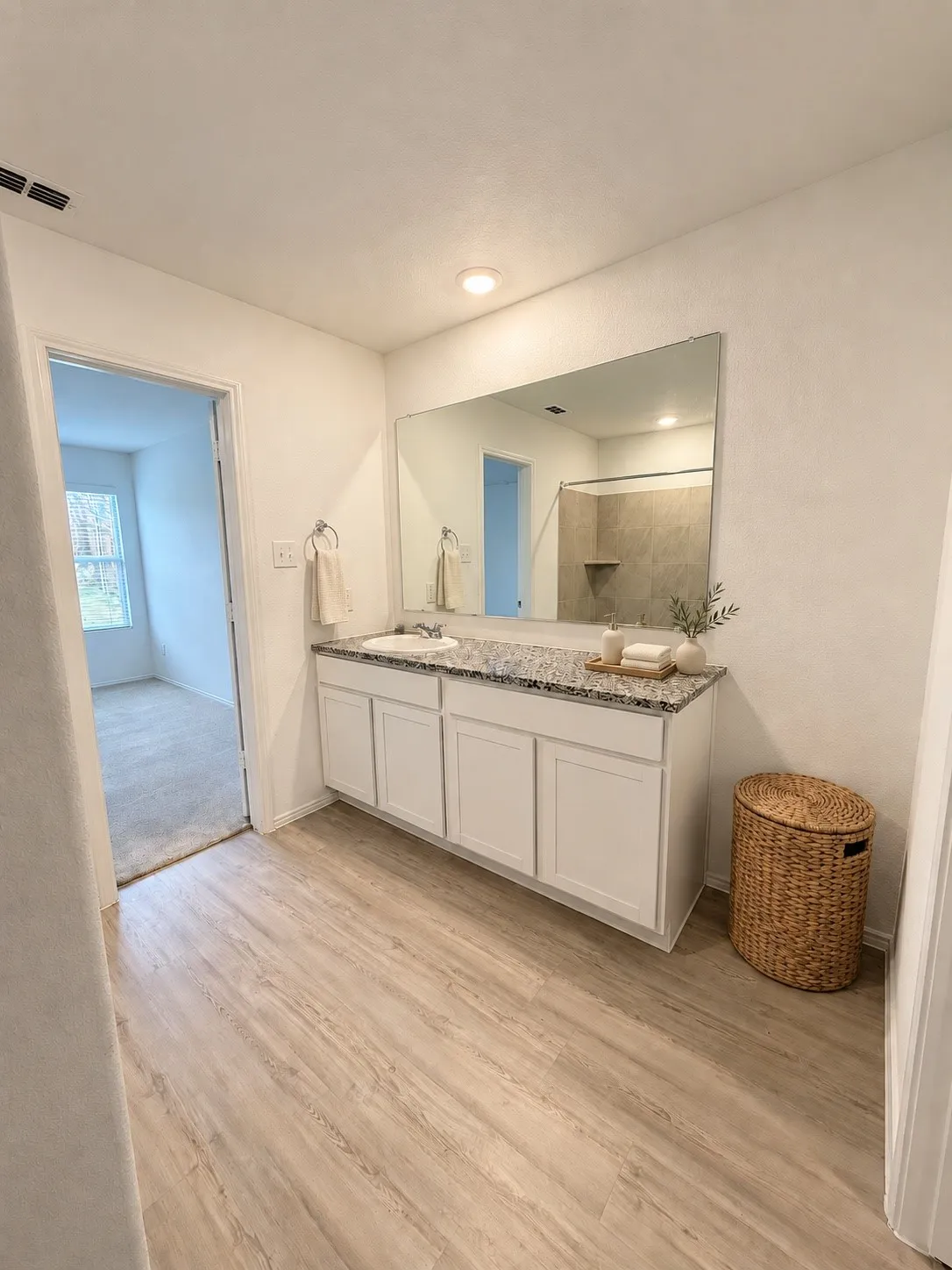 *Virtually Staged* En-suite primary bath featuring a granite countertop vanity, tiled tub and shower surround, recessed lighting, and luxury vinyl plank flooring.