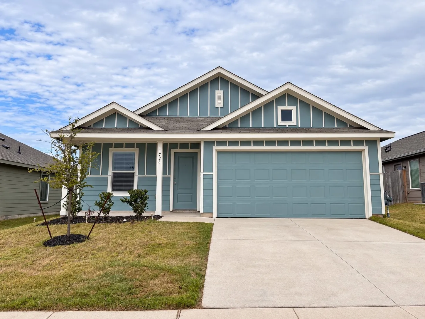 Attractive single-story home featuring blue siding with crisp white trim, an attached two-car garage, covered front entry, and landscaped front yard.