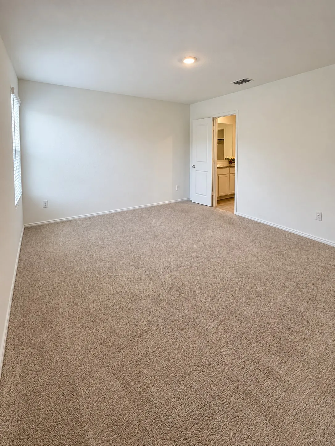 Spacious primary bedroom featuring neutral carpeting, recessed lighting, natural light, and direct access to the en-suite bathroom and walk-in closet.