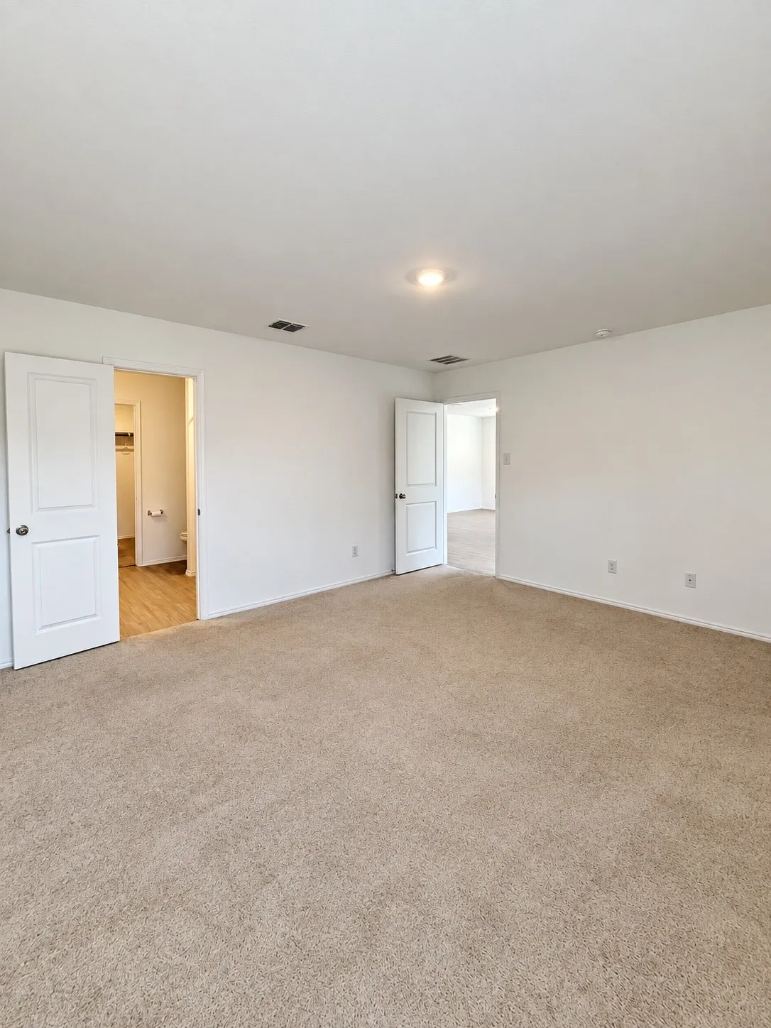 Spacious primary bedroom featuring neutral carpeting, recessed lighting, natural light, and direct access to the en-suite bathroom and walk-in closet.