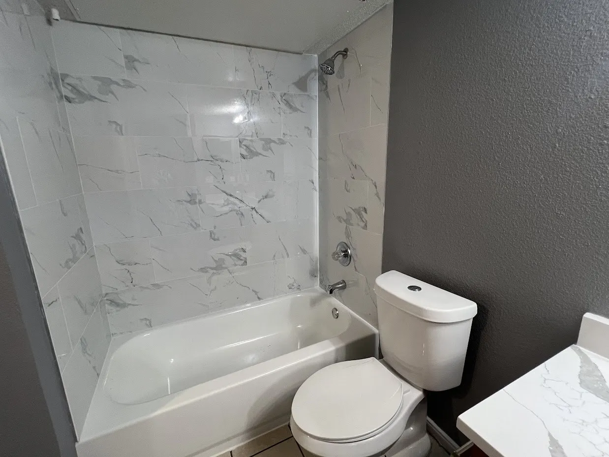 Bathtub with white and gray patterned tile surround, chrome fixtures, and a white toilet