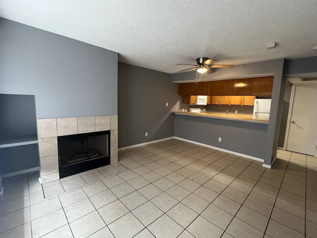 Tile flooring, fireplace with tile surround, built-in shelving, wood-finish cabinetry, and built-in ceiling fan