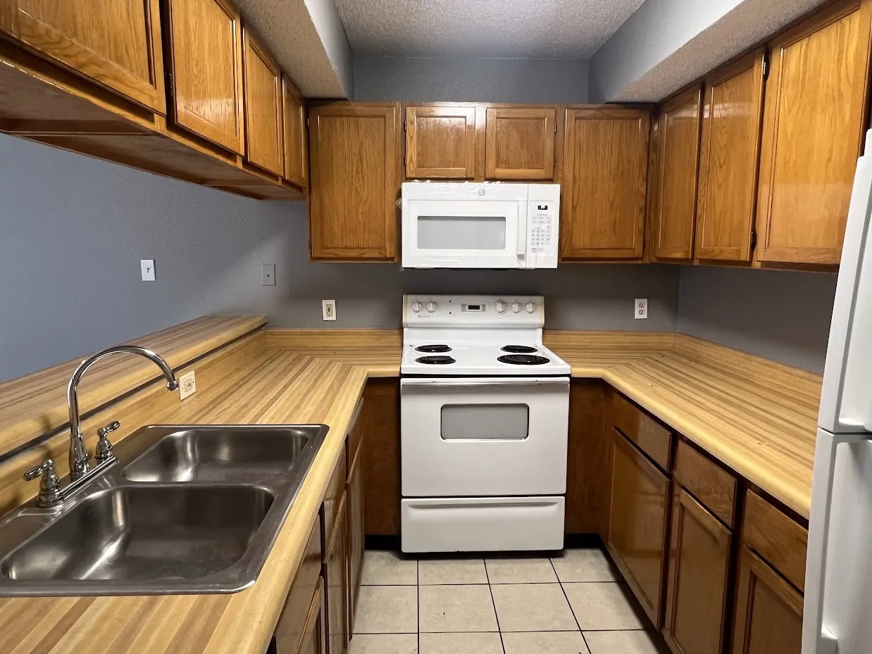 U-shaped kitchen featuring wood-finish countertops, wood cabinetry, a stainless steel double basin sink, and white appliances