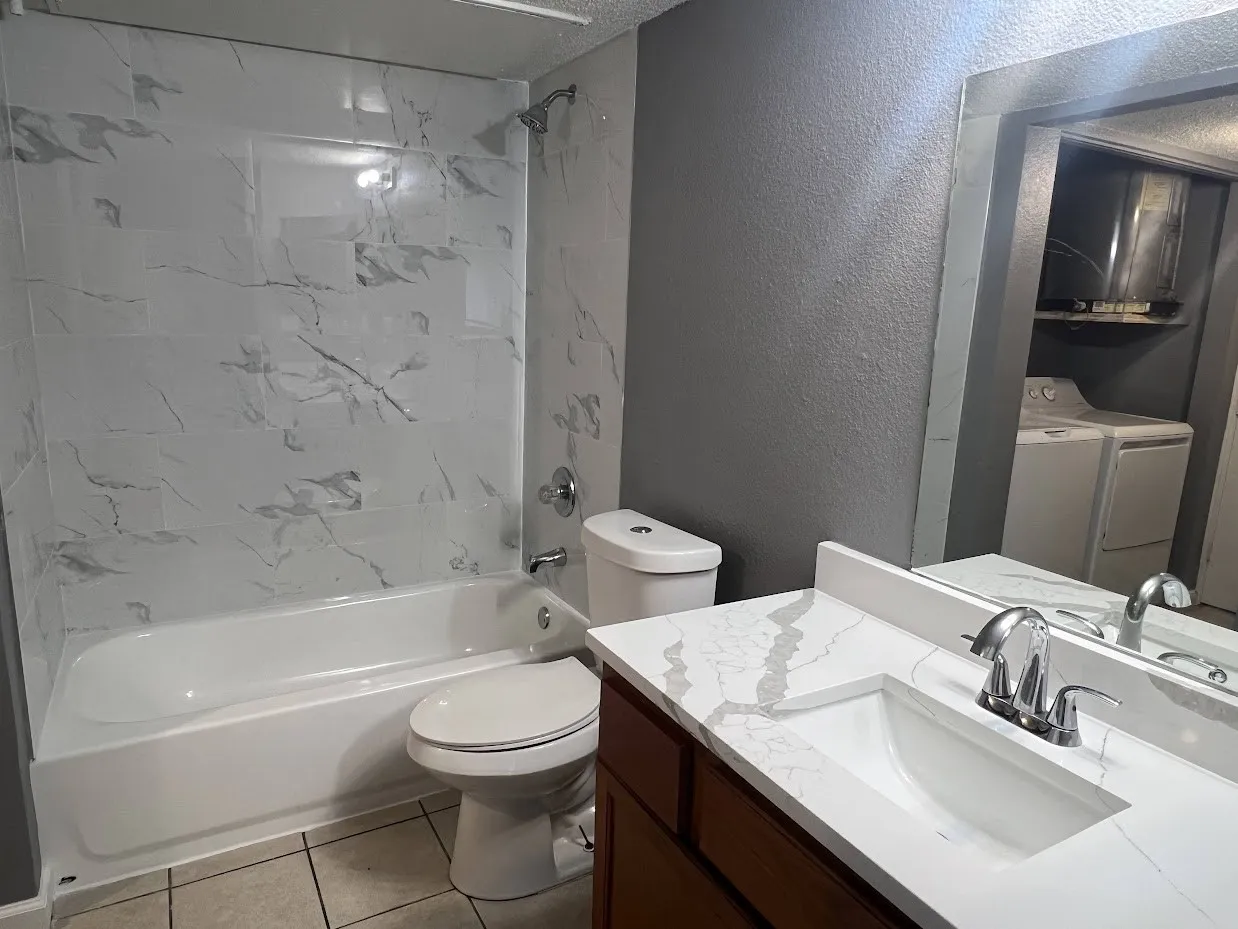 Bathroom featuring a white bathtub with a tile surround, a toilet, a vanity with a white countertop and integrated sink, and chrome fixtures