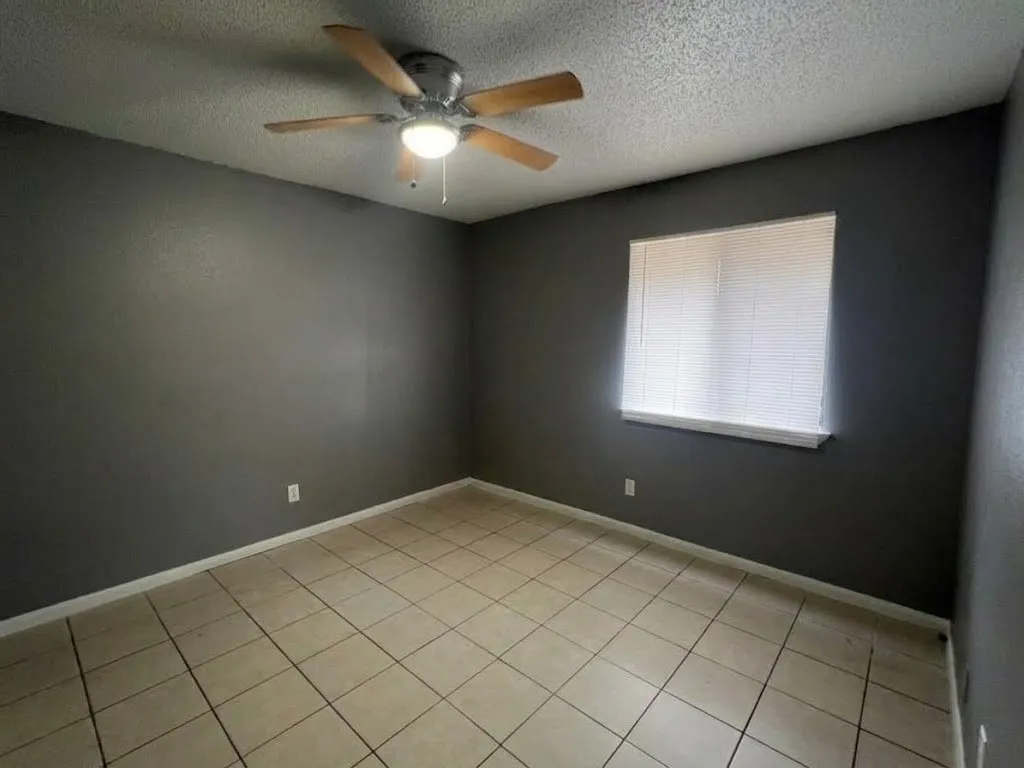 Room featuring ceramic tile flooring, a window with horizontal blinds, a ceiling fan with integrated lighting, and dark-toned walls