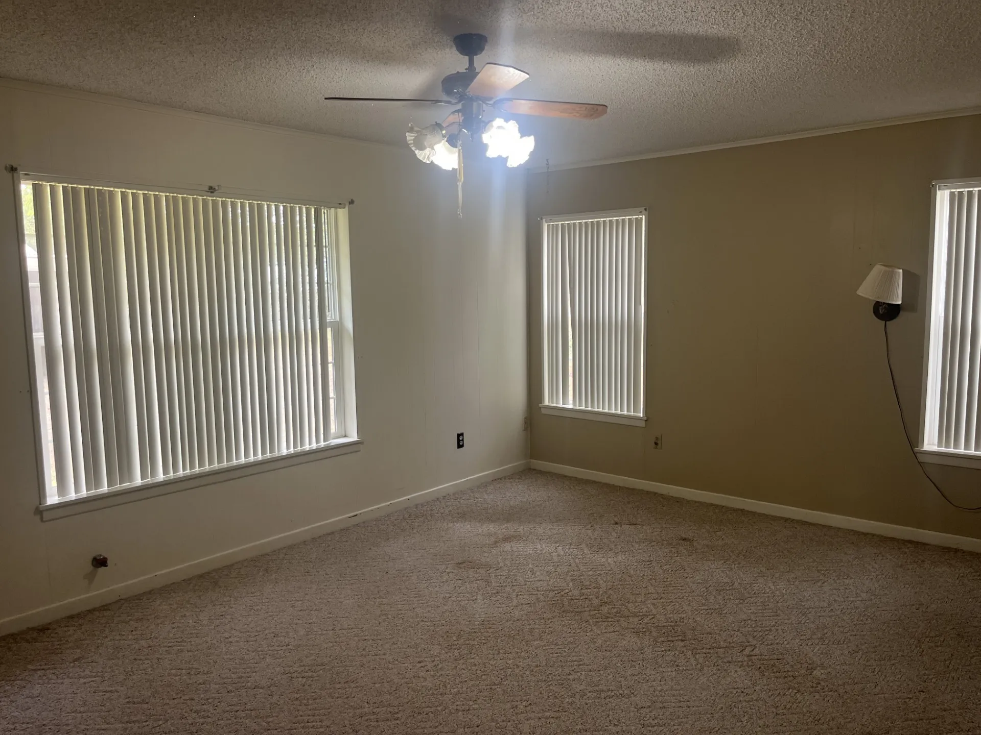 Carpeted flooring, ceiling fan with integrated lighting, multiple windows with vertical blinds, and wall-mounted sconce lighting