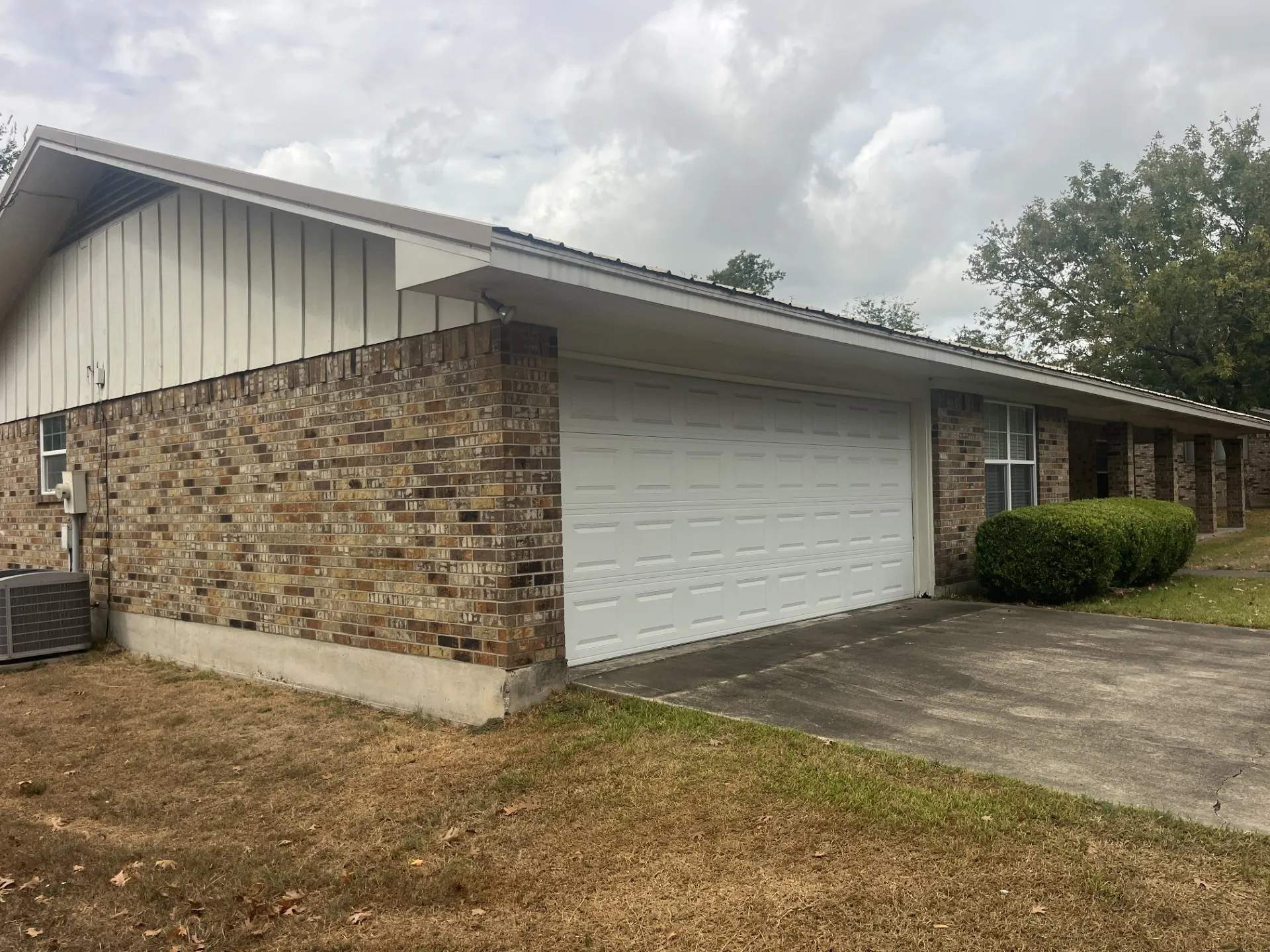 Brick exterior with a white garage door, concrete driveway, and covered entry