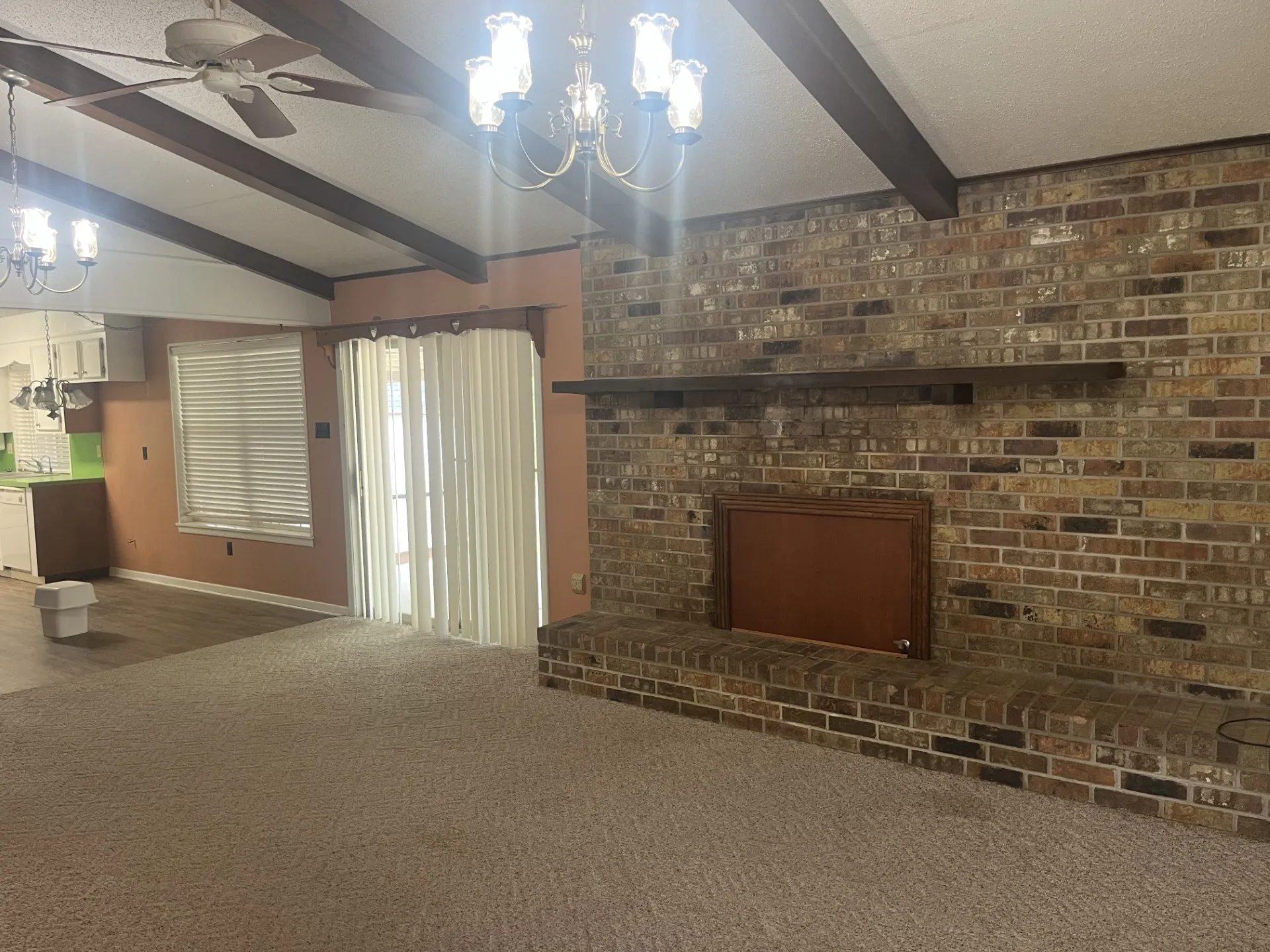 Vaulted ceiling with exposed beams, brick fireplace with a wood-finish mantel, ceiling fan, and chandelier lighting