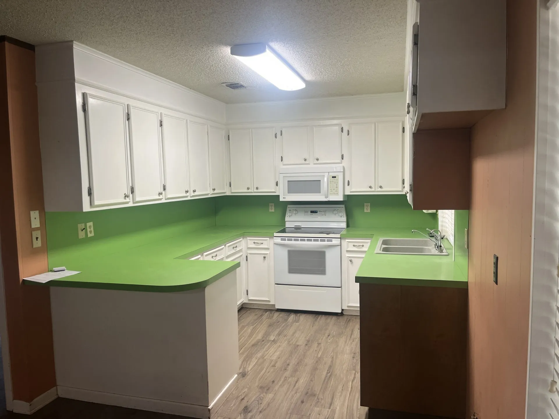 U-shaped kitchen featuring white cabinetry, green countertops, white range, white microwave, and wood-finish flooring
