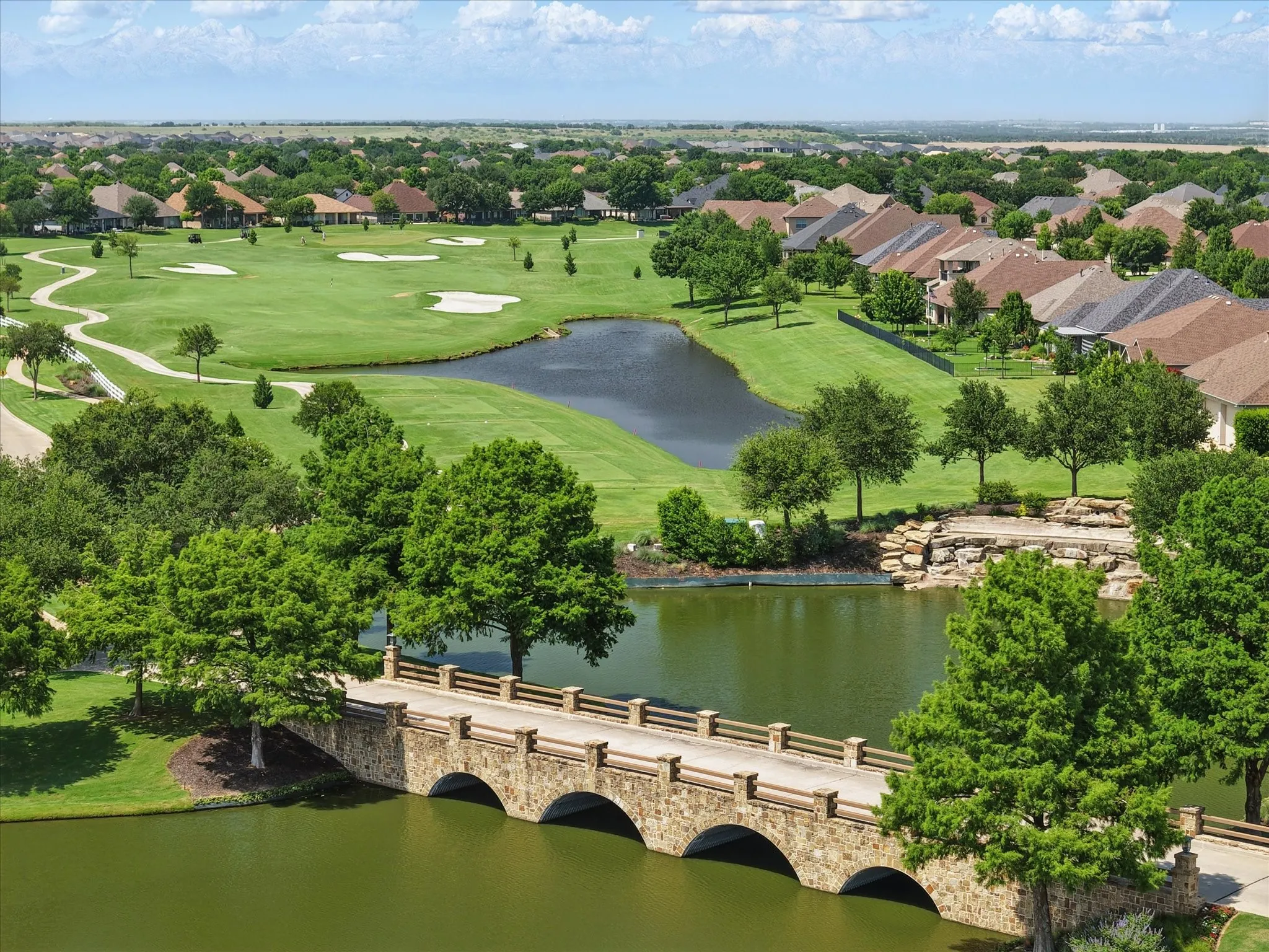 Aerial perspective of bridge, ponds, and golf course at Robson Ranch main entrance.