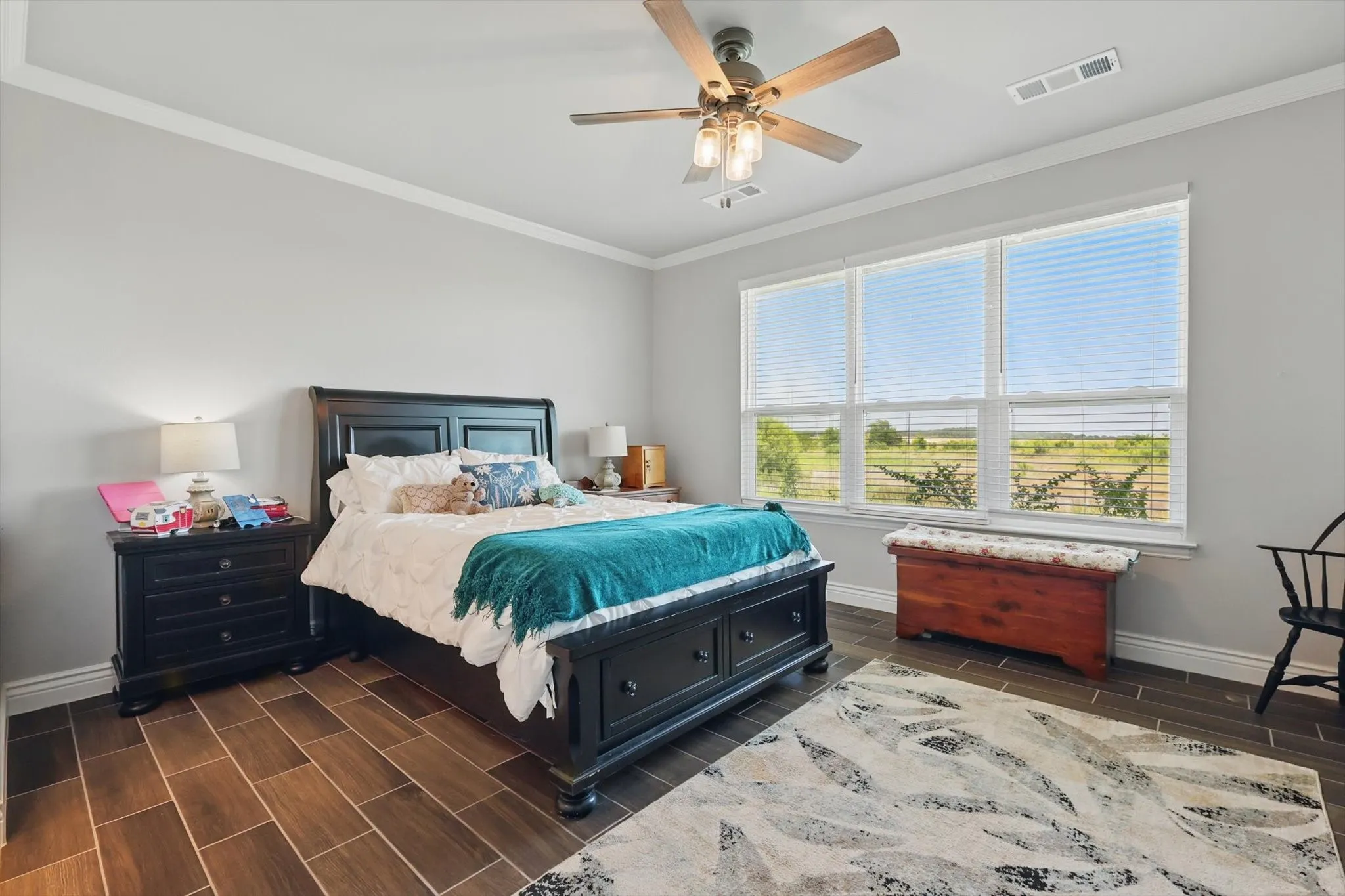 Bedroom with ornamental molding, wood tiled floors, ceiling fan, and serene views of the nature area.