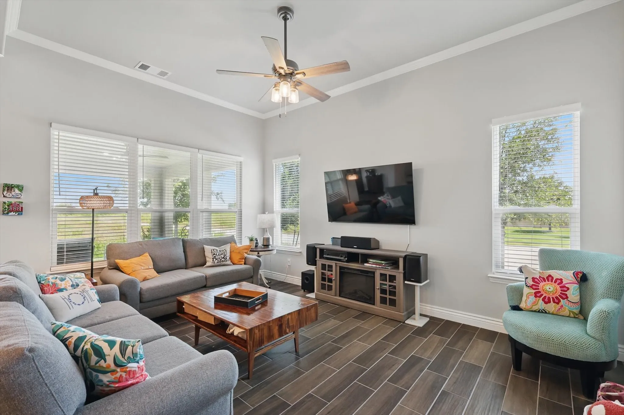 Living room featuring ornamental molding, ceiling fan, and ceramic wood-look tile.