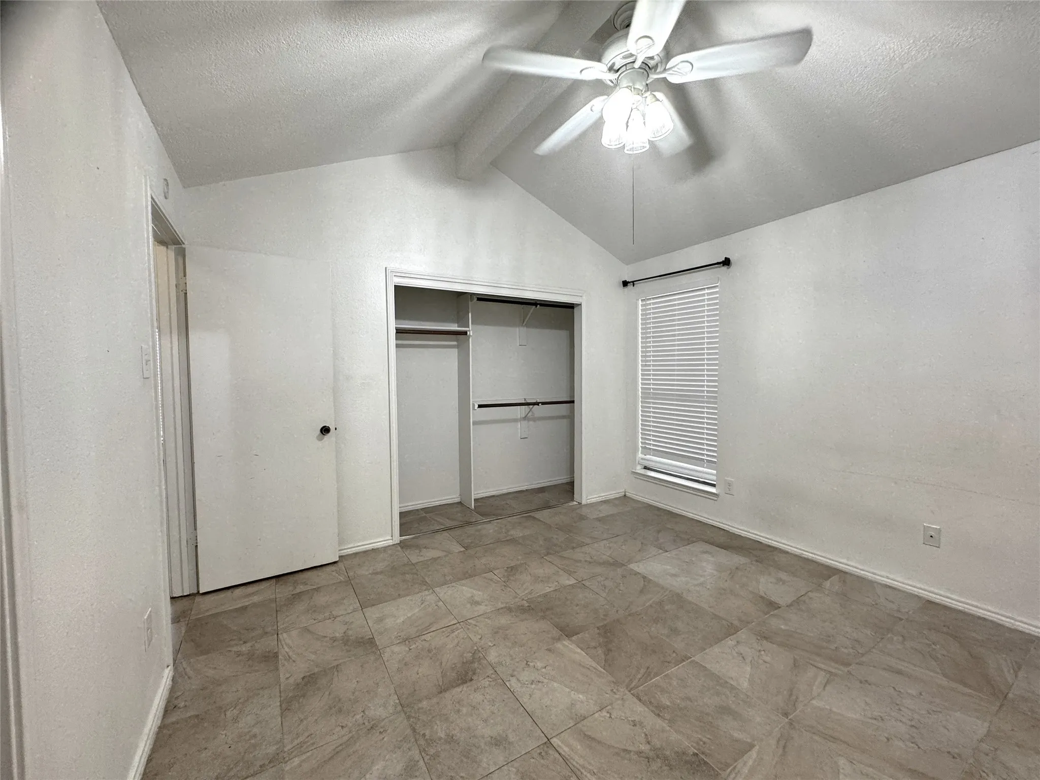Vaulted ceiling with a ceiling fan, window with blinds, tile flooring, and a built-in closet with shelving