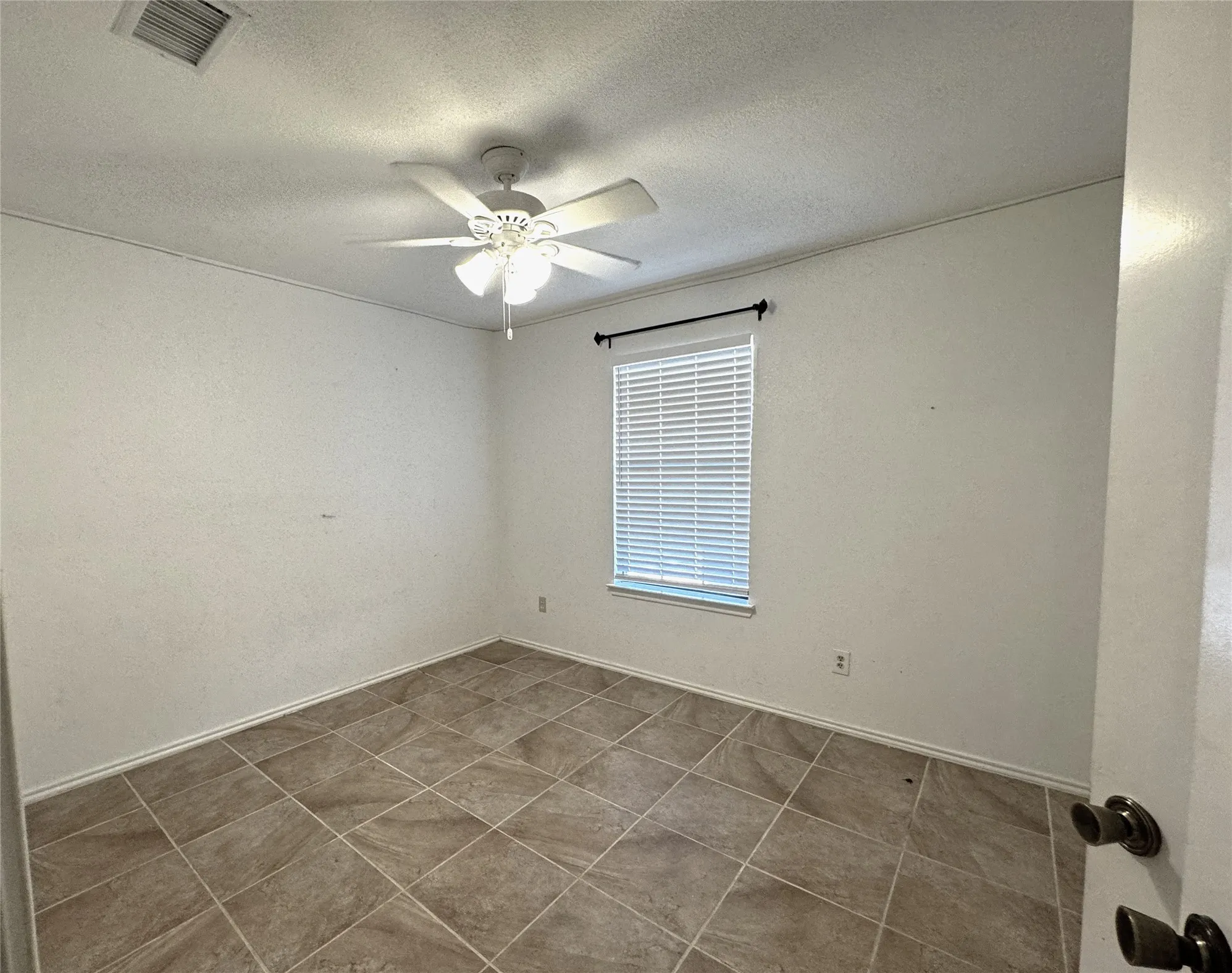 Neutral-toned tile flooring, white walls, ceiling fan with integrated lighting, and a window with blinds