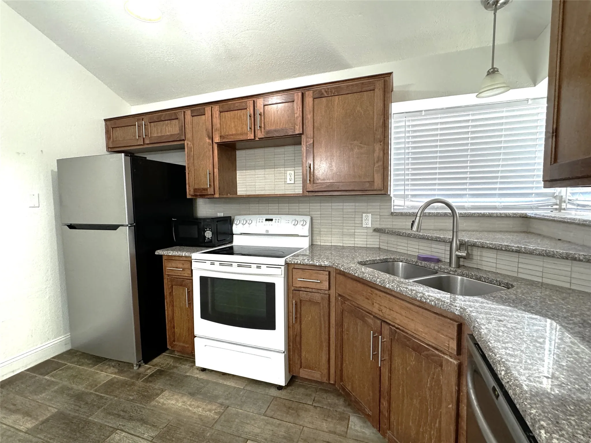 Kitchen featuring wood-finish cabinetry, granite countertops, tile backsplash, and a double basin stainless steel sink