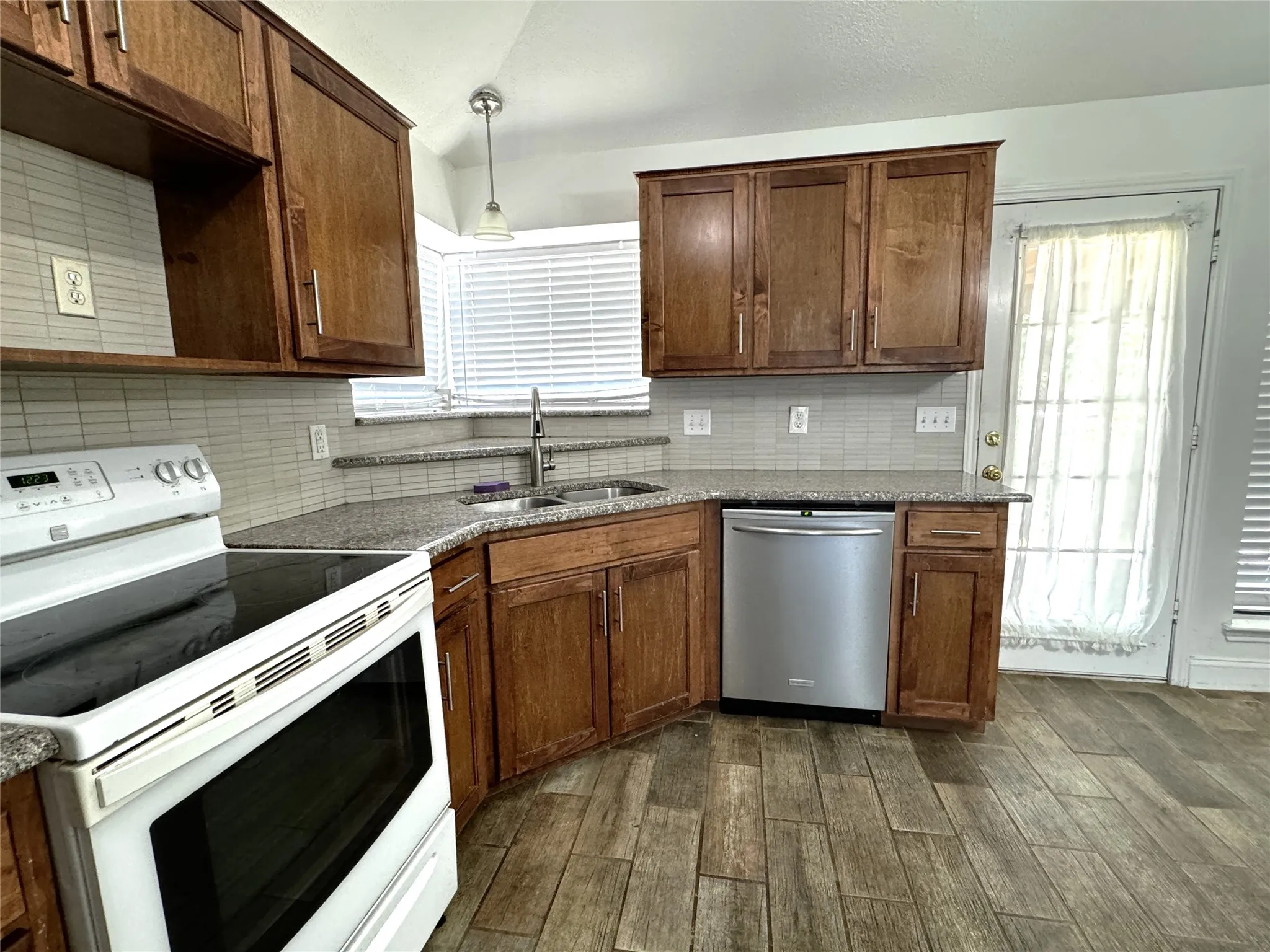 Kitchen featuring wood-finish cabinetry, speckled countertops, stainless steel dishwasher, white range, and wood-finish flooring