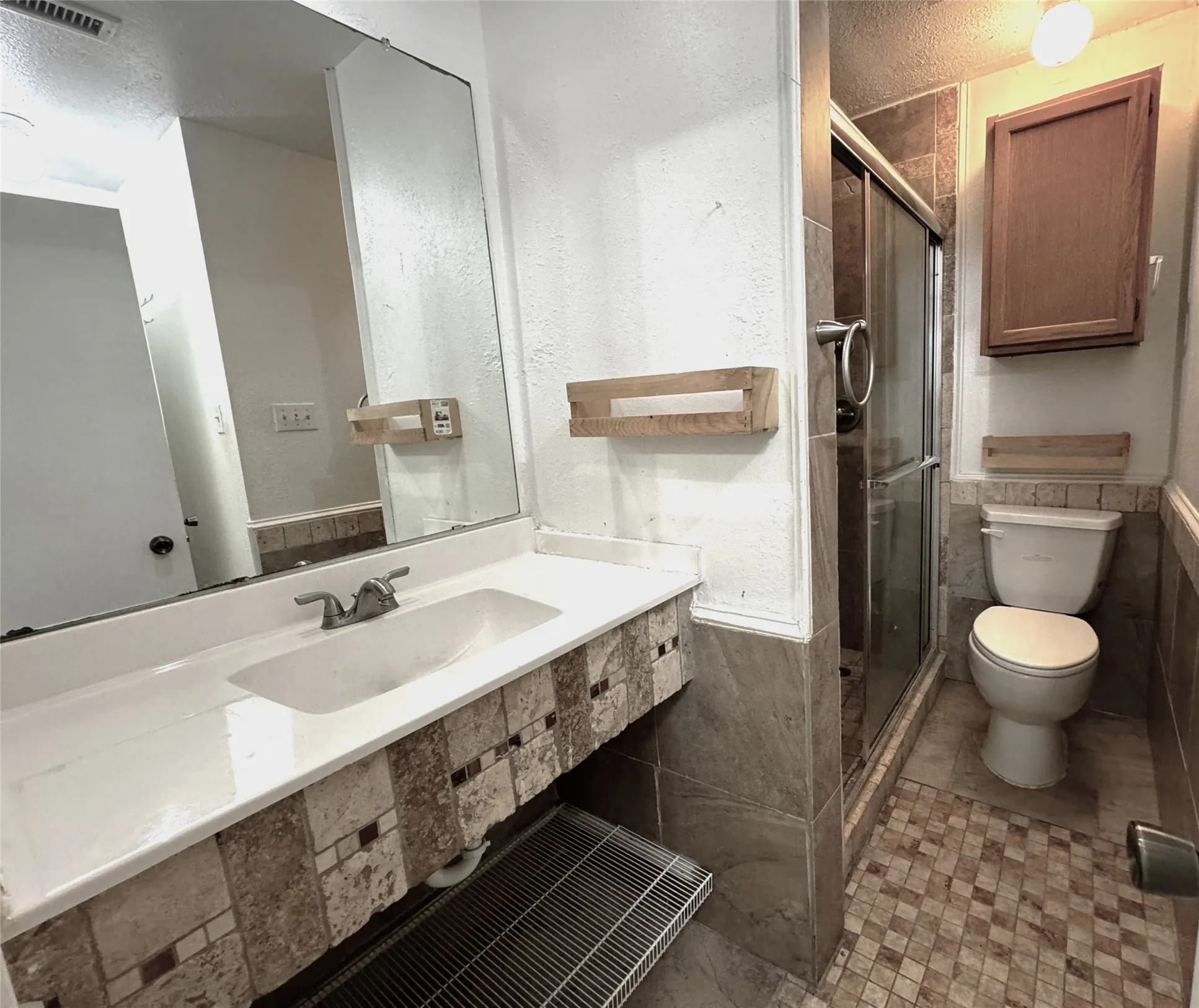 Vanity with integrated sink and mosaic tile detailing, glass-enclosed shower, wall-mounted cabinetry, and tiled flooring