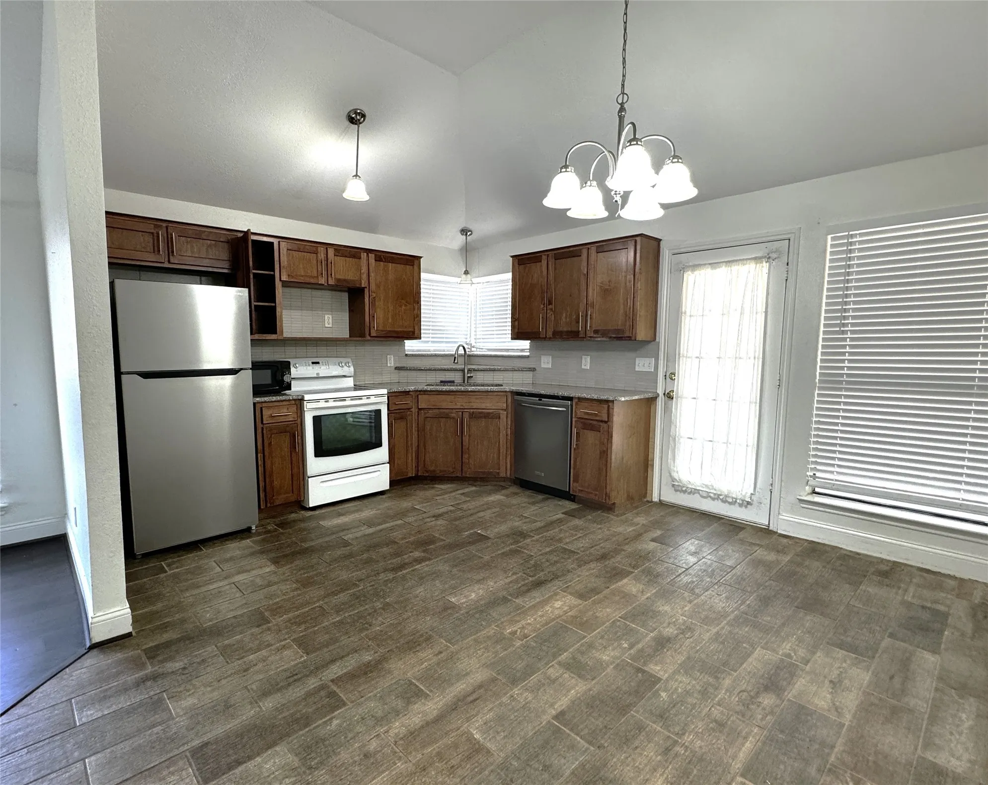 Kitchen featuring wood-finish tile flooring, vaulted ceiling, wood cabinetry, stainless steel refrigerator and dishwasher, and a white oven