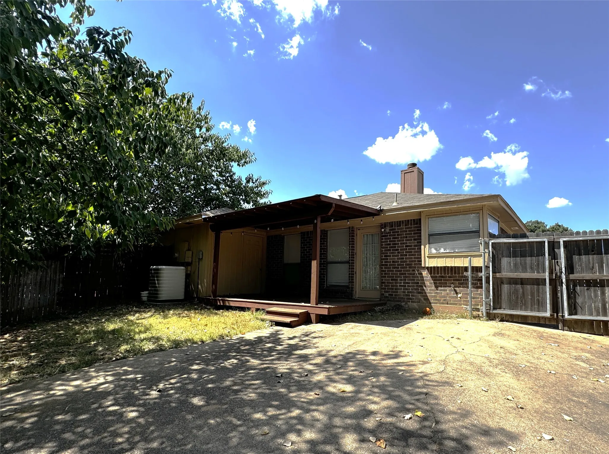 Rear brick exterior with a covered wood deck, wood fencing, and mature trees