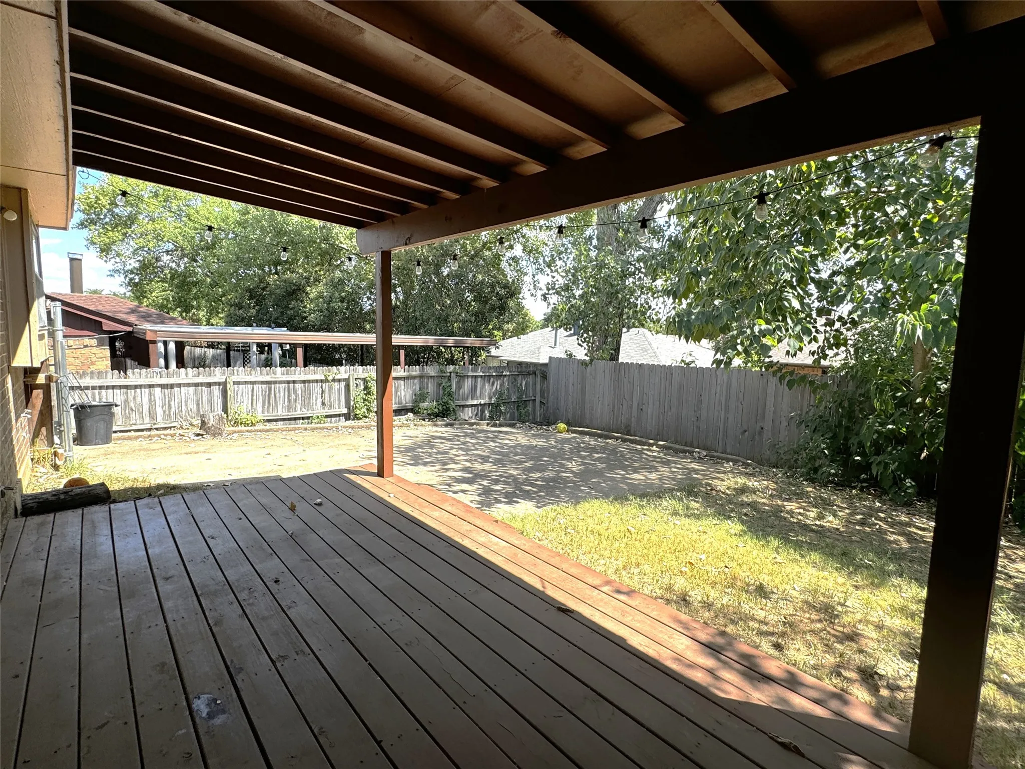 Expansive wood deck with a slatted roof overhang, wood fence perimeter, and a grass-covered backyard