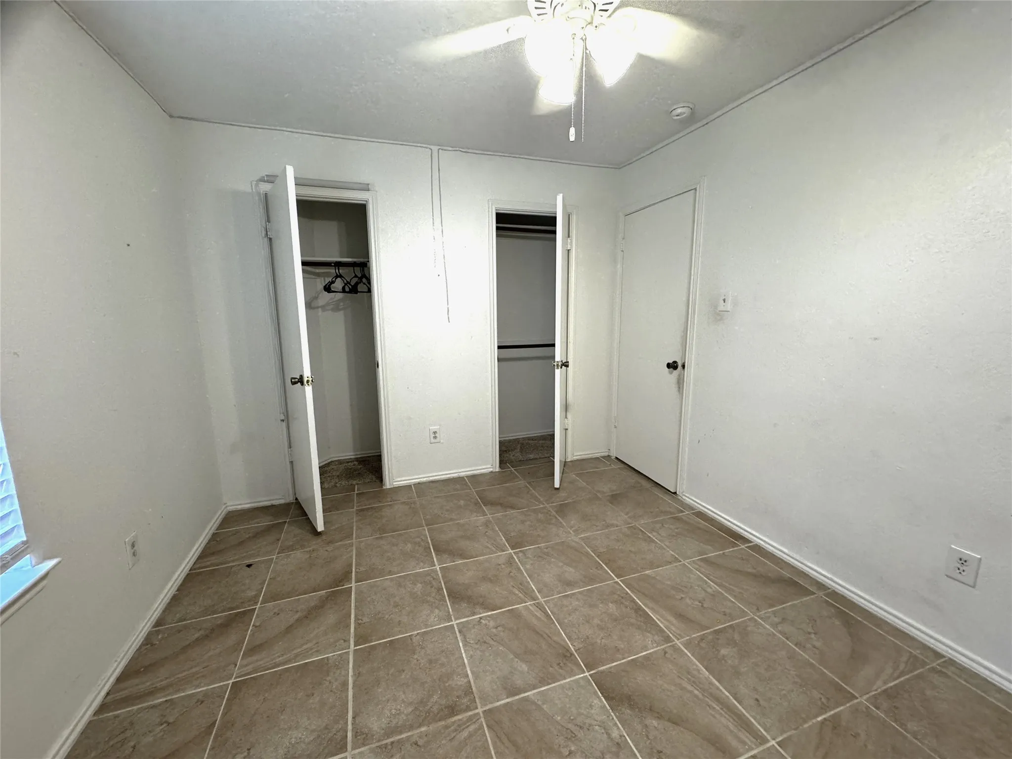 Tile flooring, white walls, built-in ceiling fan with lighting, and two built-in closets