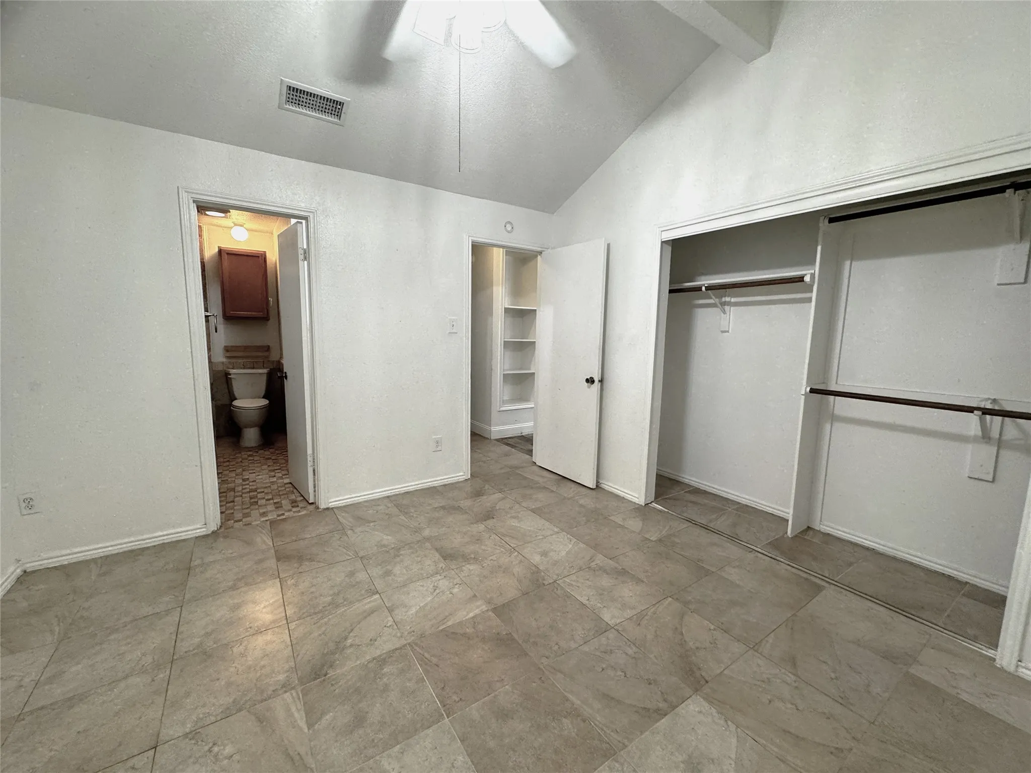Vaulted ceiling, tiled flooring, built-in shelving, and a double-door closet with hanging rods